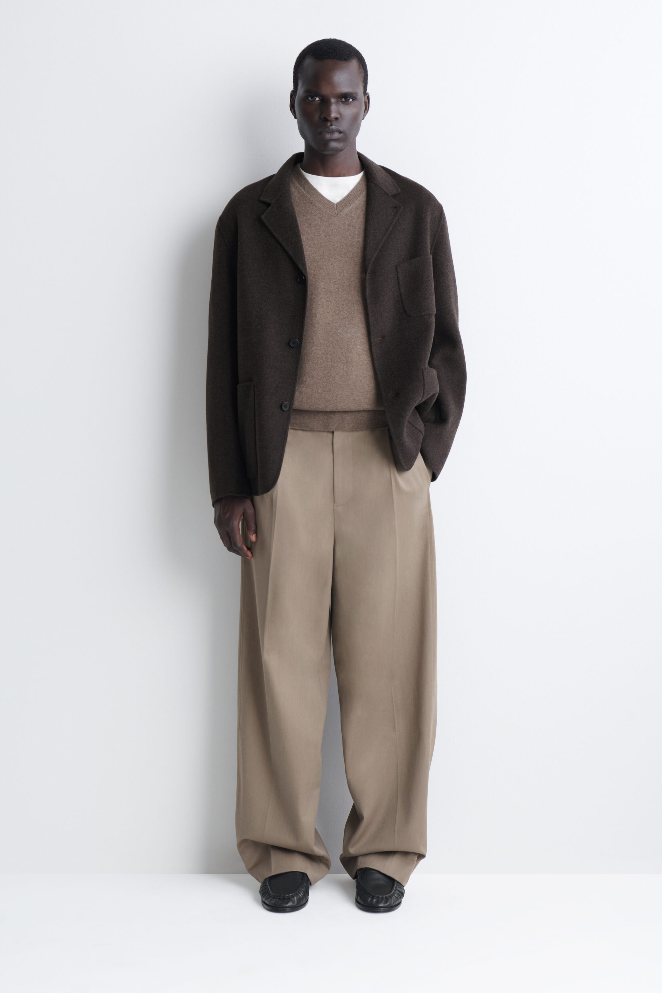 Este conjunto de frente presenta una chaqueta de lana marrón oscuro con solapas de muesca y bolsillos de parche, superpuesta sobre un jersey marrón claro de cuello en V y una camiseta blanca de cuello redondo. El look se completa con pantalones beige de pinzas y pernera ancha que caen sobre unos zapatos de cuero negro. Este conjunto de frente presenta una chaqueta de lana marrón oscuro con solapas de muesca y bolsillos de parche, superpuesta sobre un jersey marrón claro de cuello en V y una camiseta blanca de cuello redondo. El look se completa con pantalones beige de pinzas y pernera ancha que caen sobre unos zapatos de cuero negro.