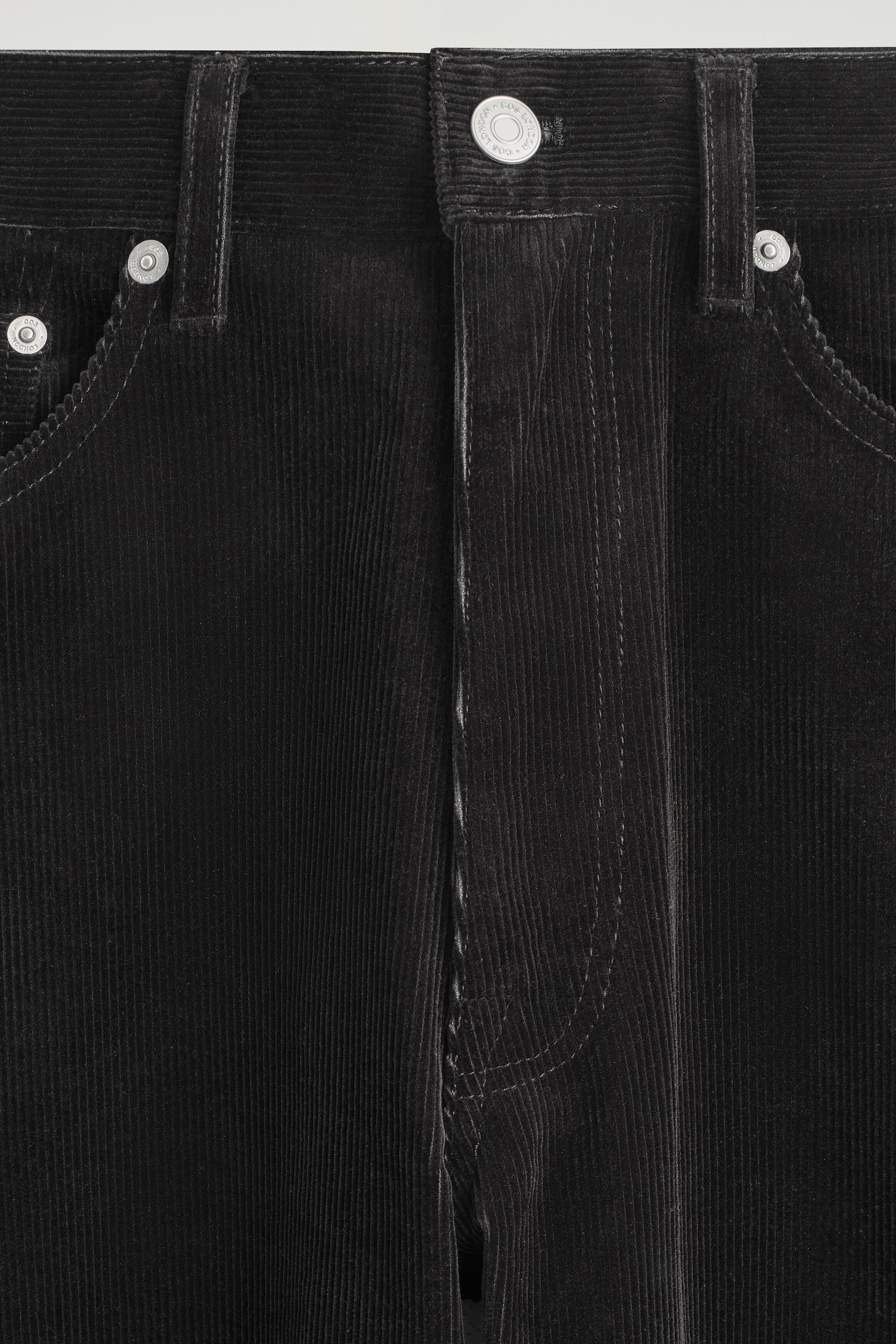 The Facade Corduroy Straight-Leg Jeans are shown in a close-up front view of the waistband, highlighting the black, fine-wale corduroy texture. This detail features a silver-tone button fastening, belt loops, and curved front pockets with silver rivet accents. The Facade Corduroy Straight-Leg Jeans are shown in a close-up front view of the waistband, highlighting the black, fine-wale corduroy texture. This detail features a silver-tone button fastening, belt loops, and curved front pockets with silver rivet accents.