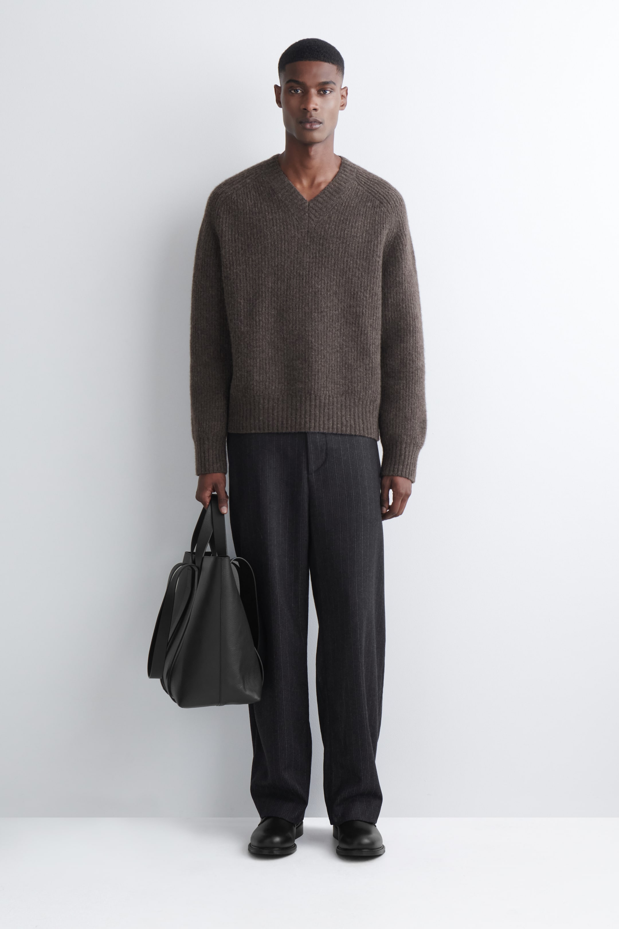 Преглед на по-голямо изображение: Тъмнокафяв пуловер с V-образно деколте е представен с лице напред. Характеризира се с вертикално оребрено плетиво с мека, четкана повърхност, както и оребрени маншети и оребрен подгъв, демонстриращи свободна кройка.