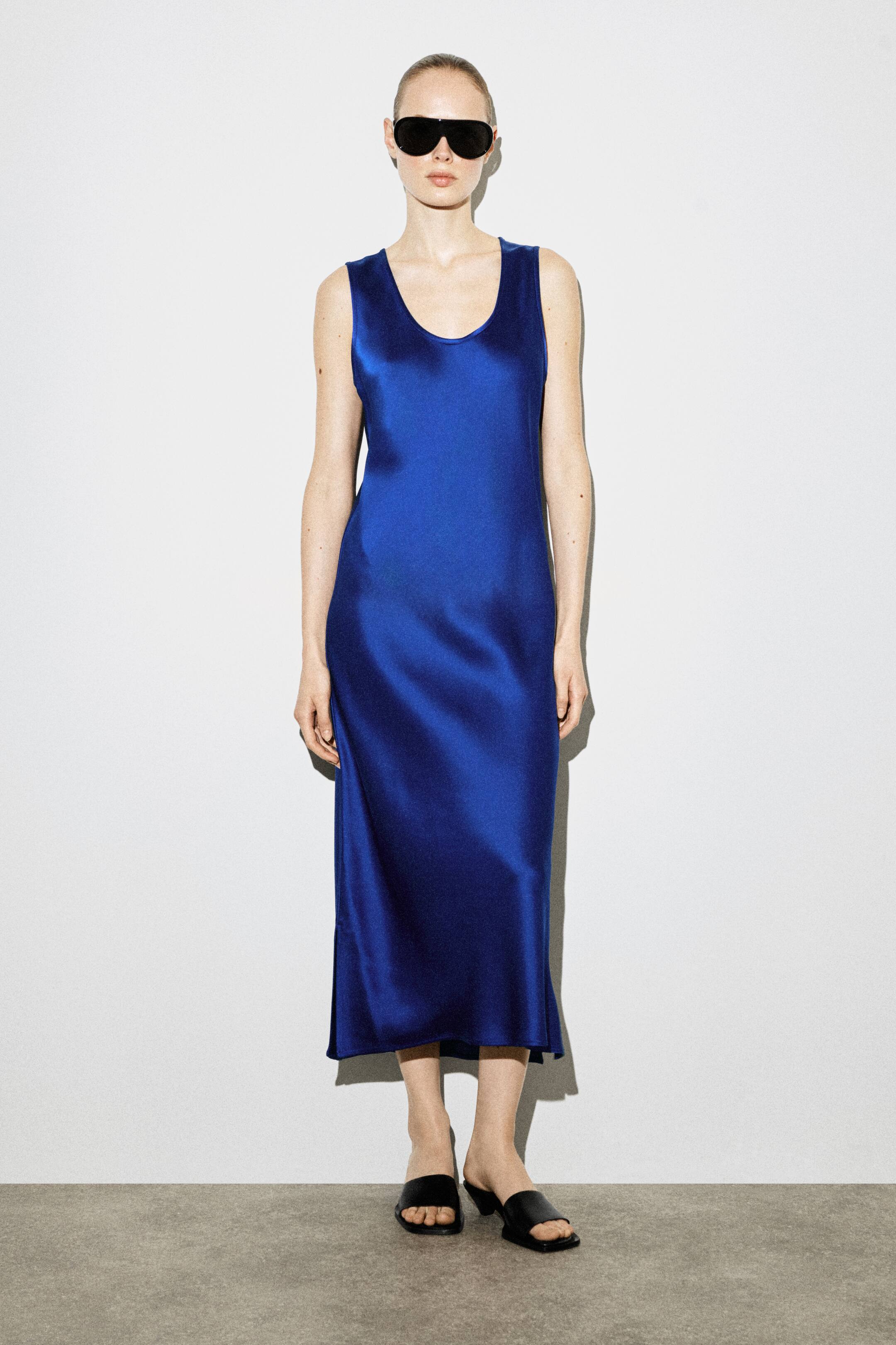 Ver imagem maior: Um vestido midi de cetim azul com decote redondo e acabamento em tecido próprio está a ser usado pela modelo. O vestido sem mangas apresenta uma silhueta reta, uma bainha fina e cai abaixo do joelho.