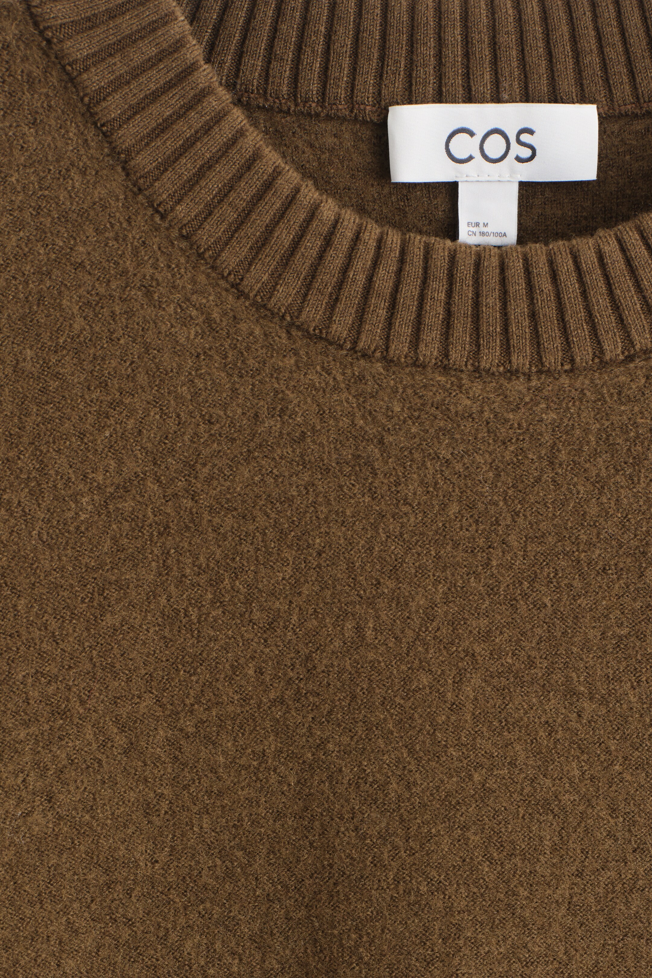 Agrandir l'image: Un pull en laine brun foncé est présenté de face, mettant en valeur un col rond avec une large bordure côtelée. Une étiquette de marque blanche est visible à l'intérieur de l'encolure.