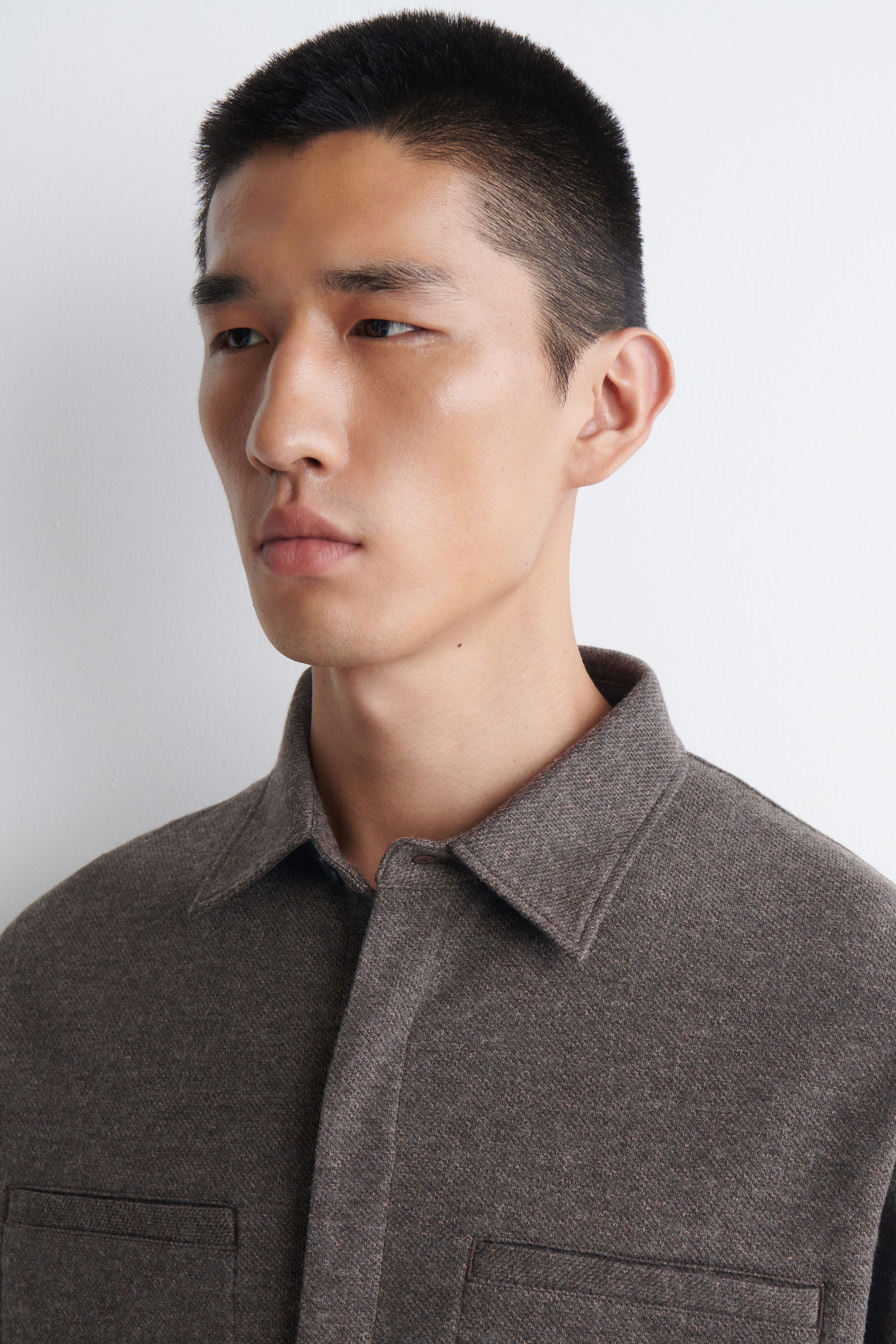 A heathered dark brown overshirt featuring a spread collar, a front placket, and two patch pockets on the chest. A heathered dark brown overshirt featuring a spread collar, a front placket, and two patch pockets on the chest.