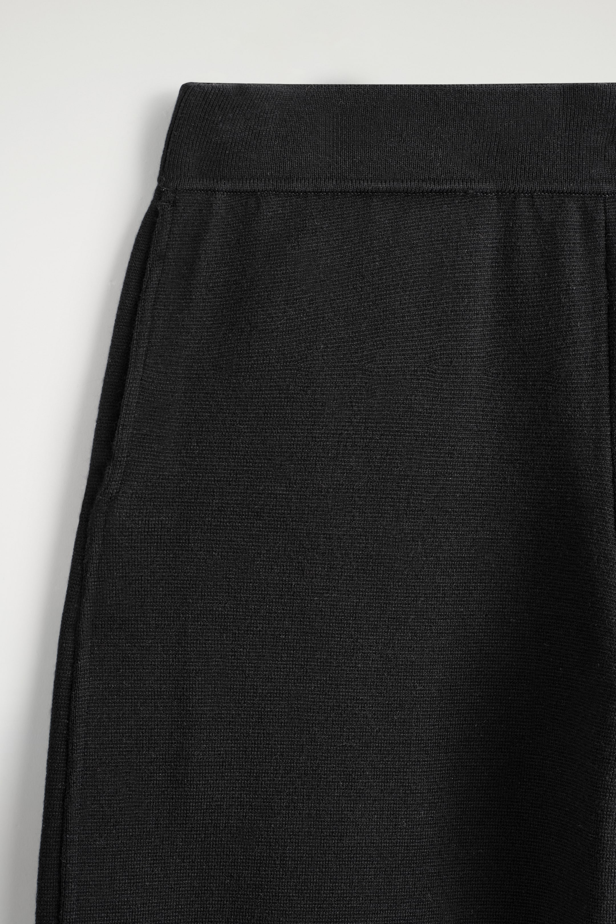 Visualizza immagine più grande: La parte superiore dei pantaloni neri a maglia è mostrata dalla parte anteriore, con una cintura liscia e tasche laterali verticali. Il tessuto presenta un motivo a maglia fine e densa.