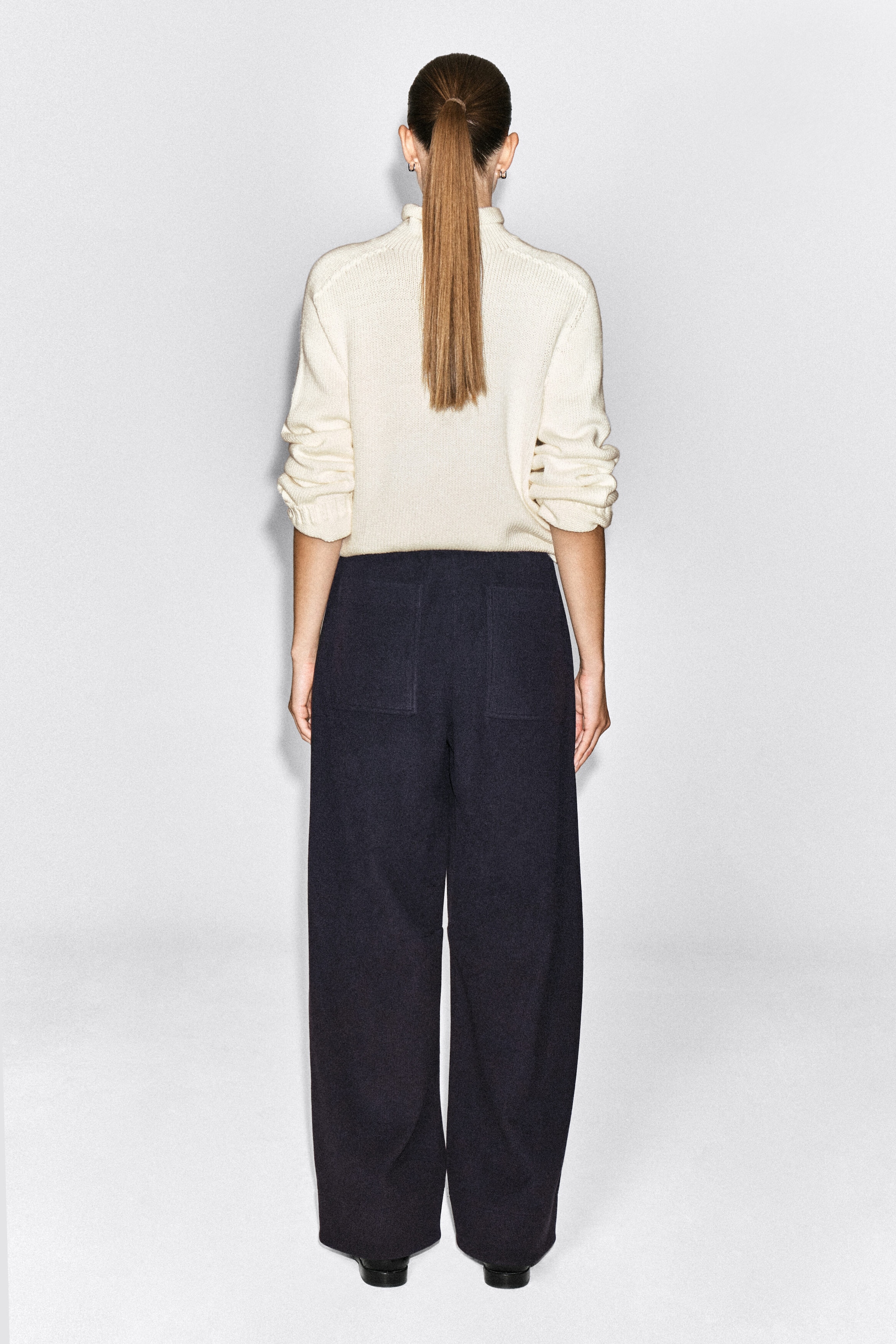 Corduroy-jersey wide-leg pants in dark navy are worn by the model, shown from the back. The pants feature a relaxed silhouette with two large rear patch pockets and are paired with a cream-colored knit sweater.