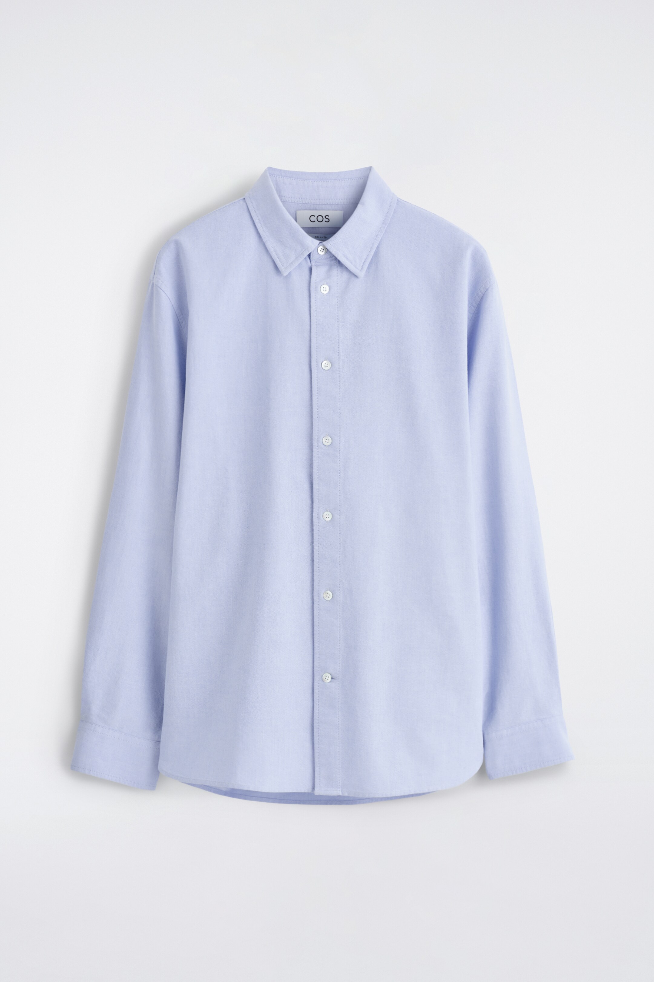 Ver imagen más grande: Una camisa azul claro se presenta como FRONT, con un cuello en punta y un cierre de botones con botones blancos en la parte delantera. Está diseñada con mangas largas, puños lisos y un dobladillo curvado.