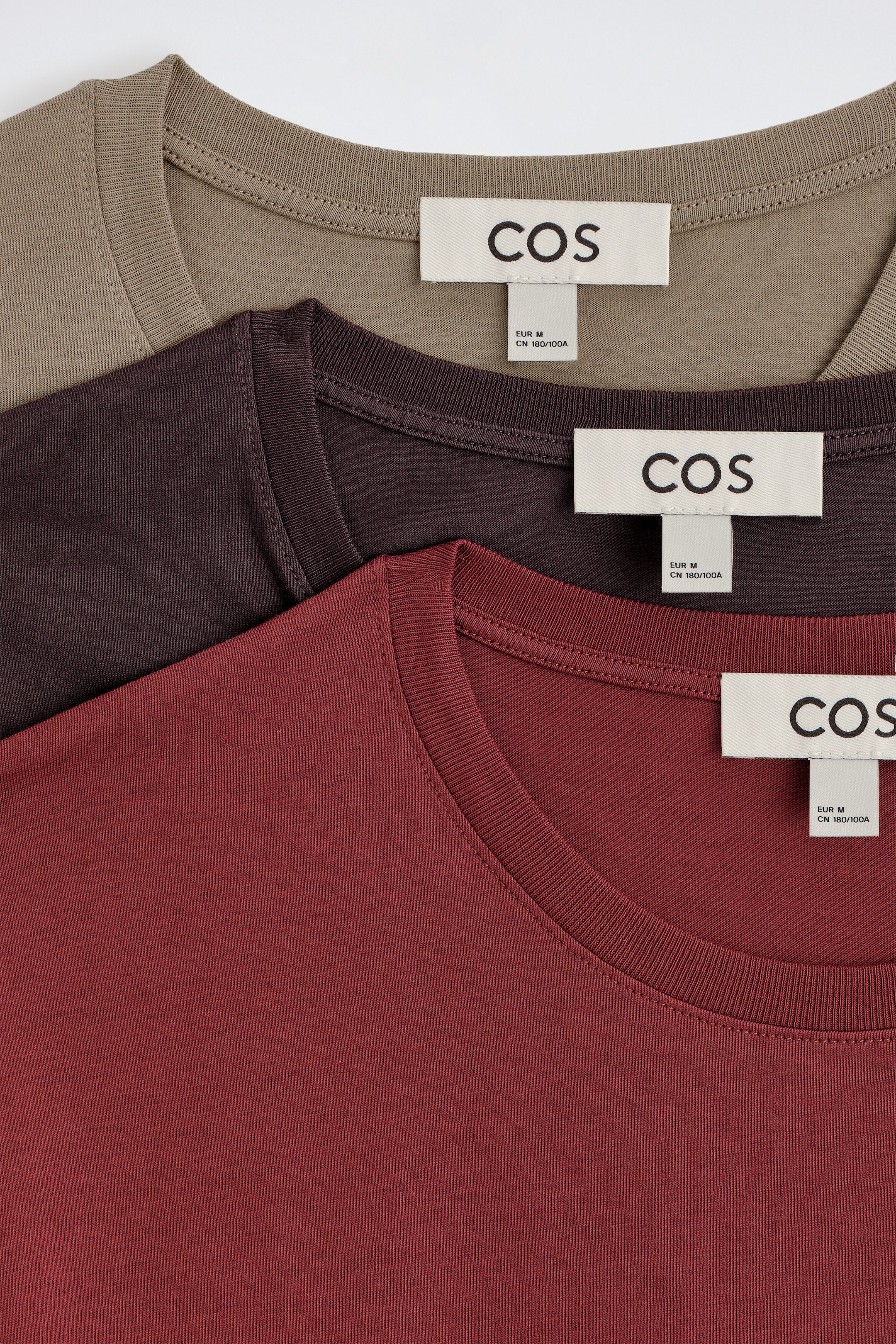 Trois t-shirts à col rond en coton, de couleur taupe, prune foncé et bordeaux, sont superposés dans une présentation en couches, mettant en valeur leurs encolures rondes côtelées et leurs étiquettes de marque intérieures, vus de face. Trois t-shirts à col rond en coton, de couleur taupe, prune foncé et bordeaux, sont superposés dans une présentation en couches, mettant en valeur leurs encolures rondes côtelées et leurs étiquettes de marque intérieures, vus de face.
