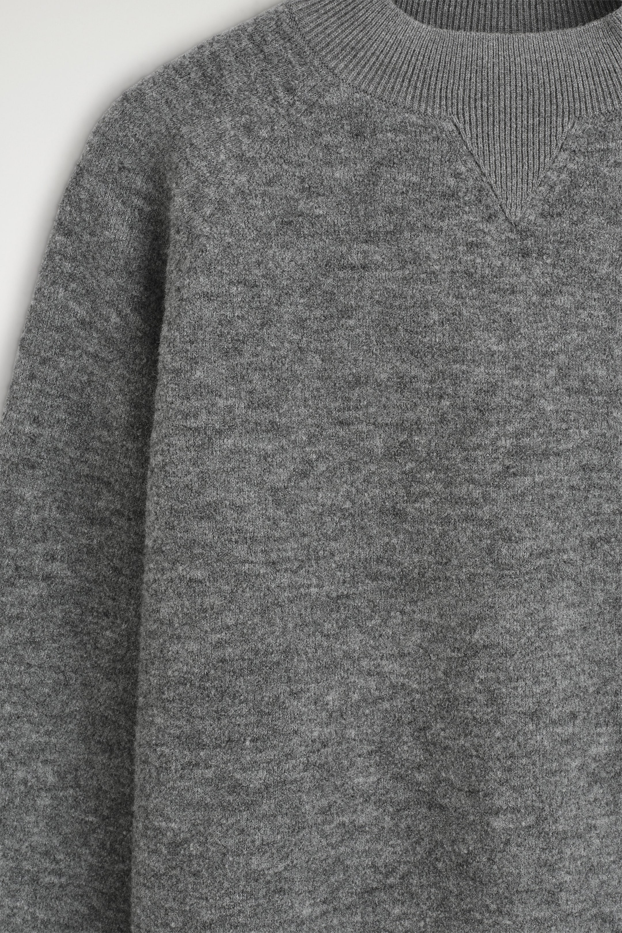 A gray knitted sweater is shown in a close-up front view, highlighting its textured bouclé fabric, with a ribbed mock neck and tonal V-insert. A gray knitted sweater is shown in a close-up front view, highlighting its textured bouclé fabric, with a ribbed mock neck and tonal V-insert.
