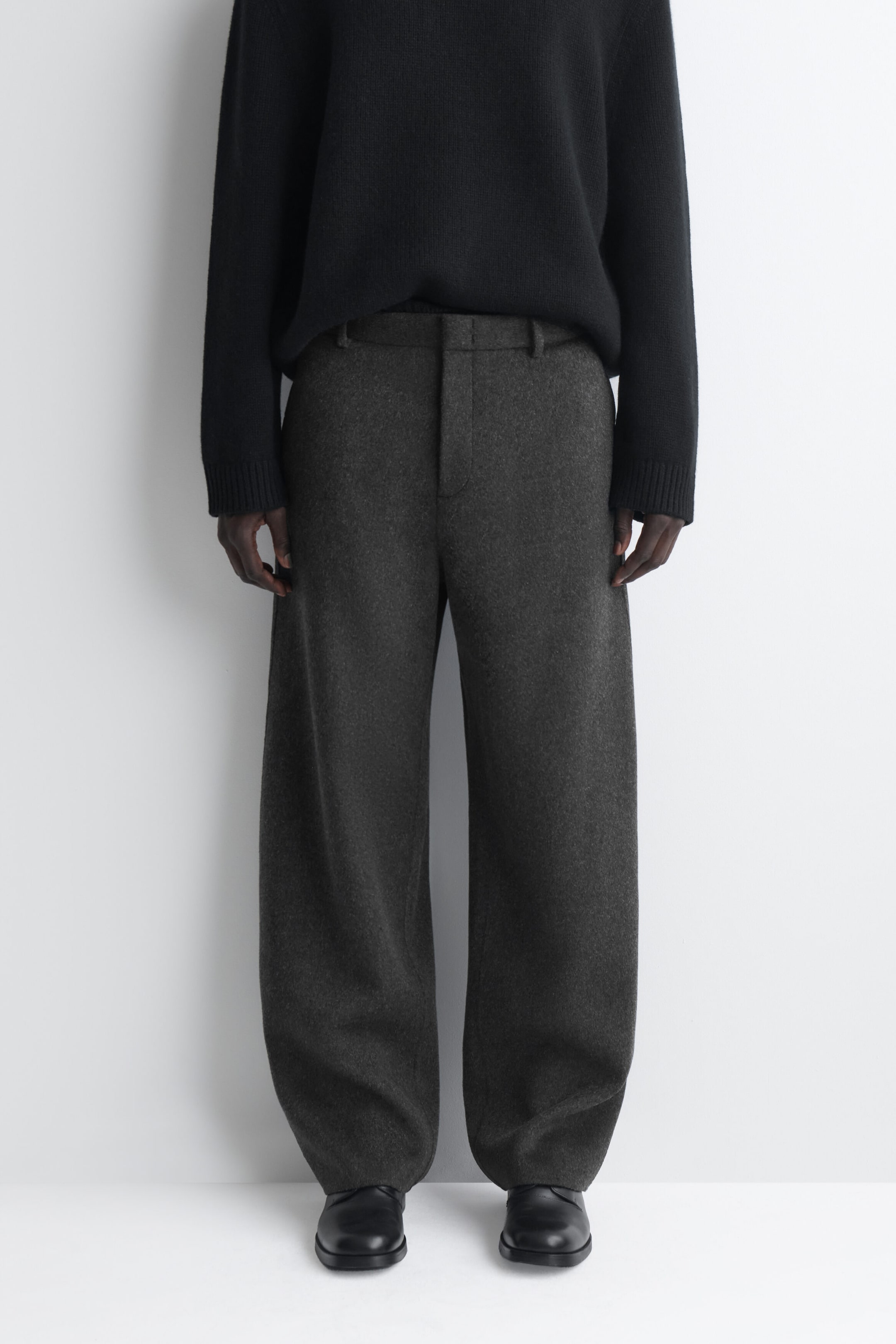 Mit einer Vorderansicht gezeigt, präsentieren sich diese dunkelgrauen, doppelseitigen Wollhosen im Relaxed-Fit und mit weitem Bein mit einem strukturierten Bund mit Gürtelschlaufen und verdecktem Verschluss. Die weite Silhouette fällt locker bis zu den schwarzen Lederschuhen und liegt dort leicht auf, während ein schwarzer Strickpullover vorne in den Bund gesteckt ist. Mit einer Vorderansicht gezeigt, präsentieren sich diese dunkelgrauen, doppelseitigen Wollhosen im Relaxed-Fit und mit weitem Bein mit einem strukturierten Bund mit Gürtelschlaufen und verdecktem Verschluss. Die weite Silhouette fällt locker bis zu den schwarzen Lederschuhen und liegt dort leicht auf, während ein schwarzer Strickpullover vorne in den Bund gesteckt ist.