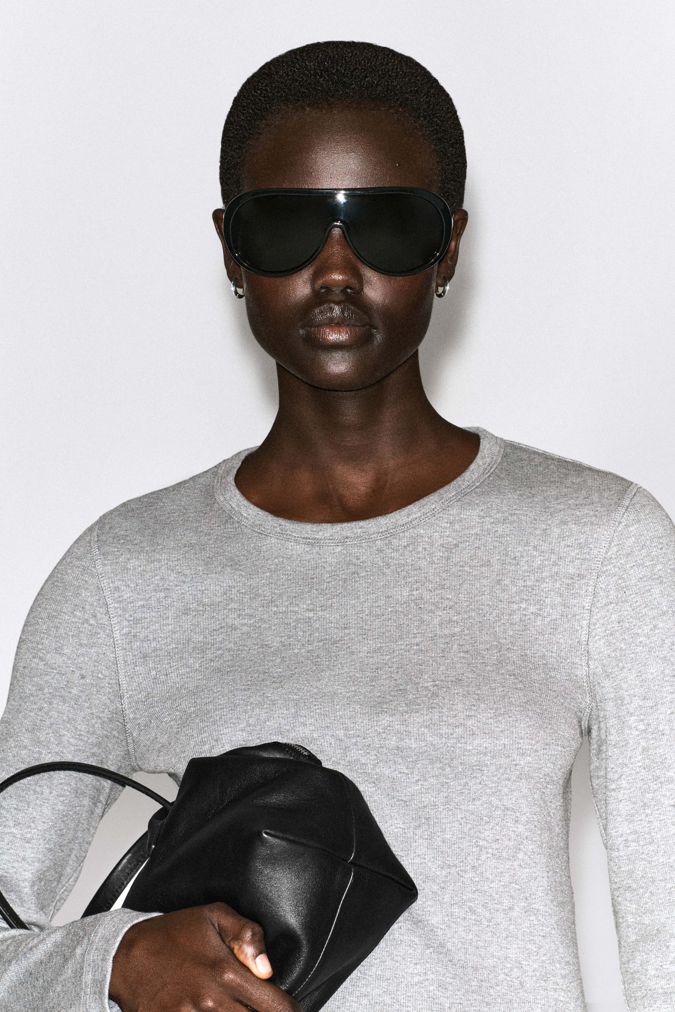 A slim ribbed cotton long-sleeve top in heather grey is shown from the front, highlighting its fine rib-knit texture and classic crew neckline. The form-fitting top contours the torso, with a black leather bag held across the front. A slim ribbed cotton long-sleeve top in heather grey is shown from the front, highlighting its fine rib-knit texture and classic crew neckline. The form-fitting top contours the torso, with a black leather bag held across the front.