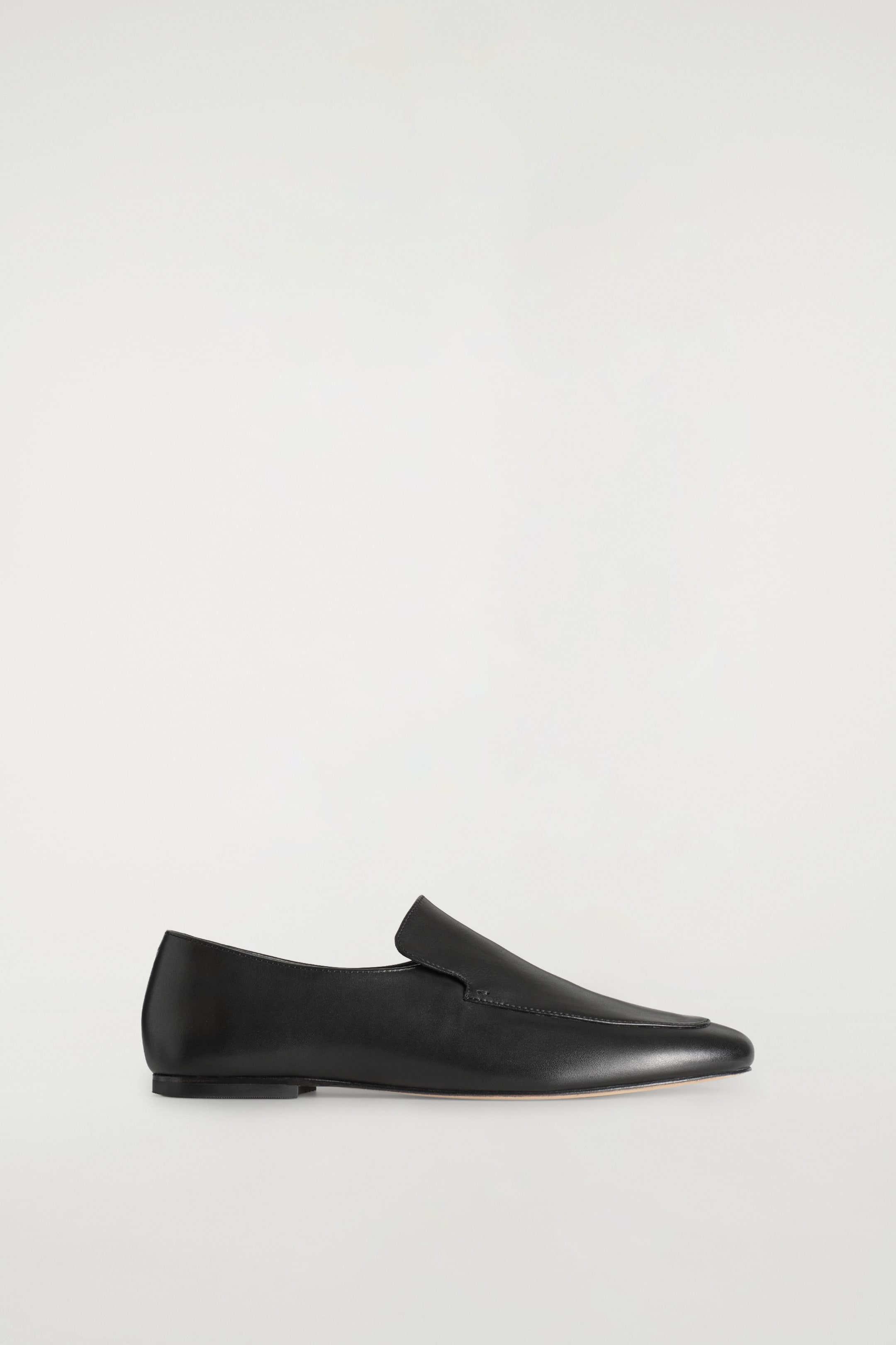 Agrandir l'image: Un mocassin en cuir noir lisse est présenté de profil, orienté vers la droite. Il présente un bout légèrement pointu, un petit talon plat et des détails de couture sur le plateau.