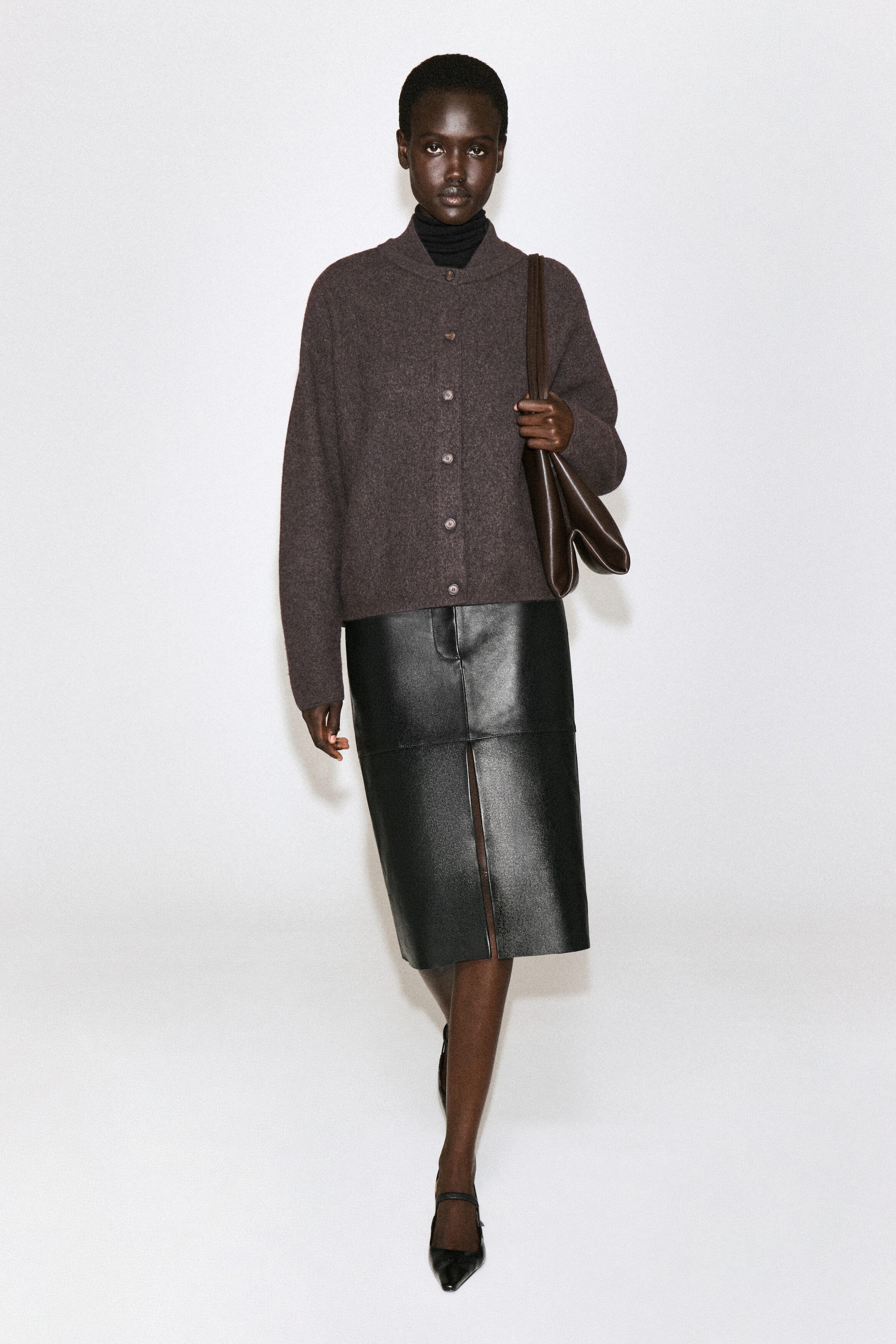 Un cardigan en laine bouillie brun foncé est présenté de face, avec une silhouette doucement arrondie, une fermeture à boutons sur le devant et un col de style bomber à effet superposé porté par-dessus un col roulé noir. Un cardigan en laine bouillie brun foncé est présenté de face, avec une silhouette doucement arrondie, une fermeture à boutons sur le devant et un col de style bomber à effet superposé porté par-dessus un col roulé noir.