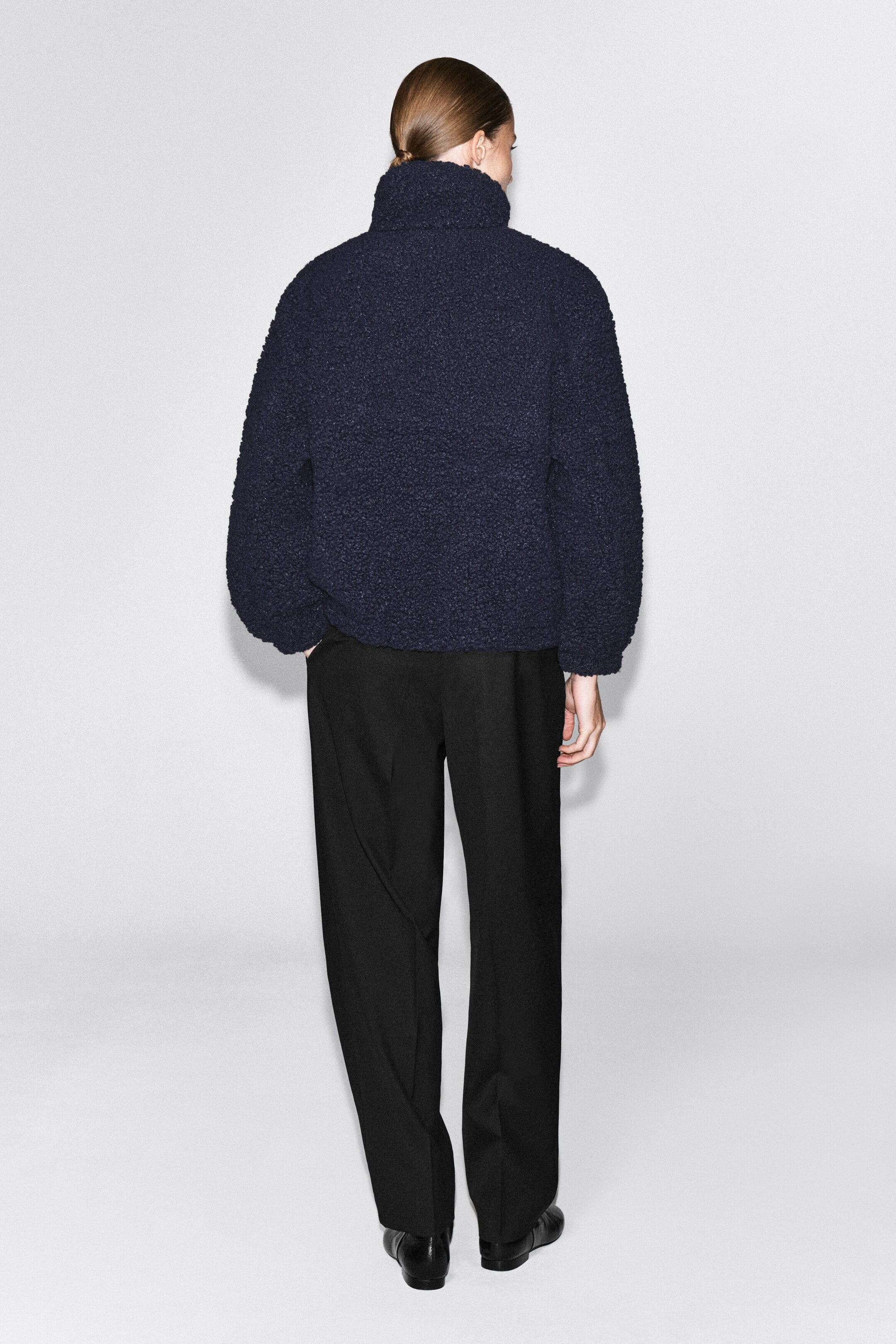 A dark navy teddy fleece jumper featuring a high funnel neck is worn by the model and shown from the back. The textured, relaxed-fit garment is styled with black trousers. A dark navy teddy fleece jumper featuring a high funnel neck is worn by the model and shown from the back. The textured, relaxed-fit garment is styled with black trousers.