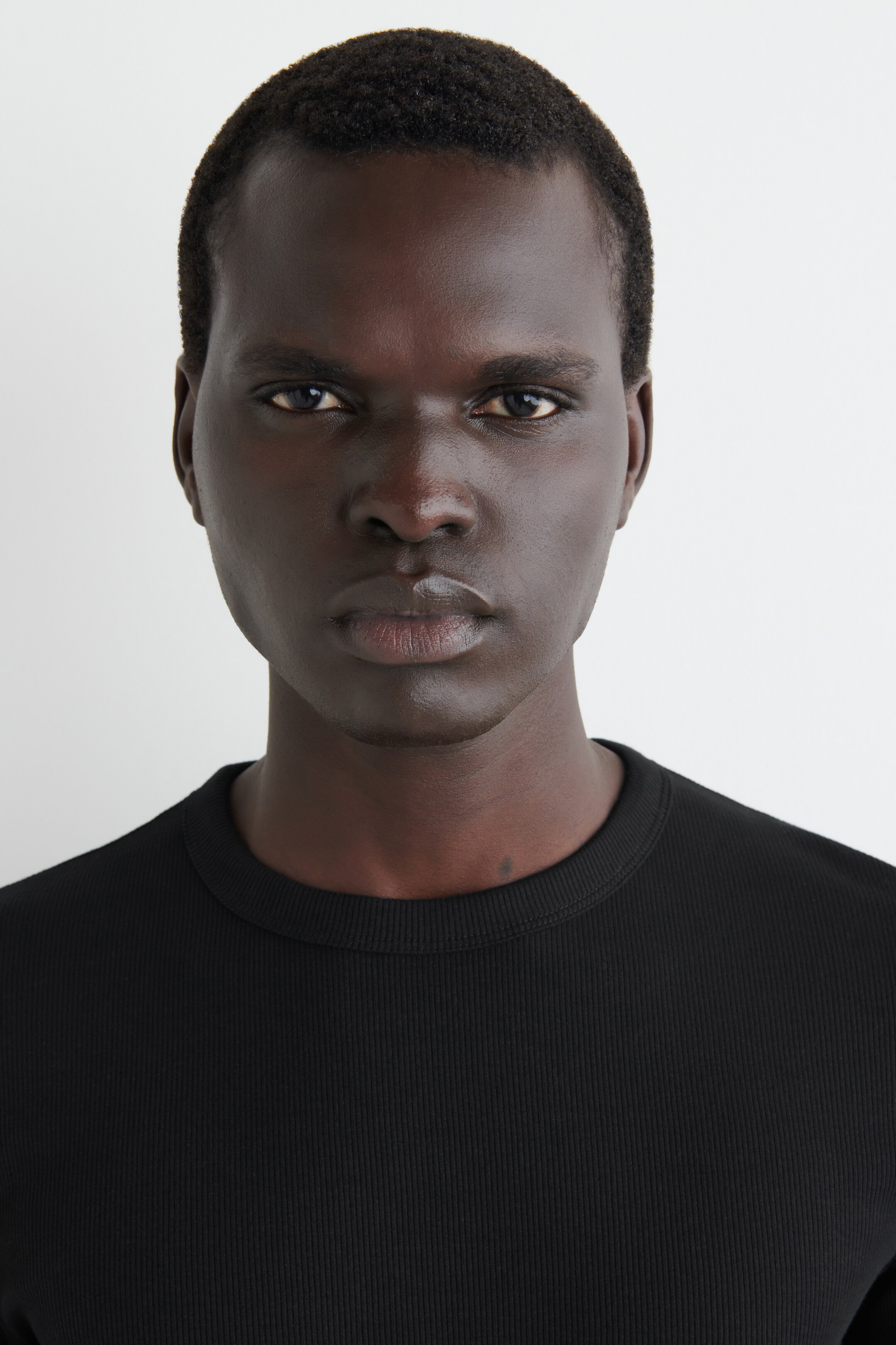Ver imagen más grande: Se lleva una camiseta negra de cuello redondo acanalado, con la tela ajustada visible en el pecho y los hombros.