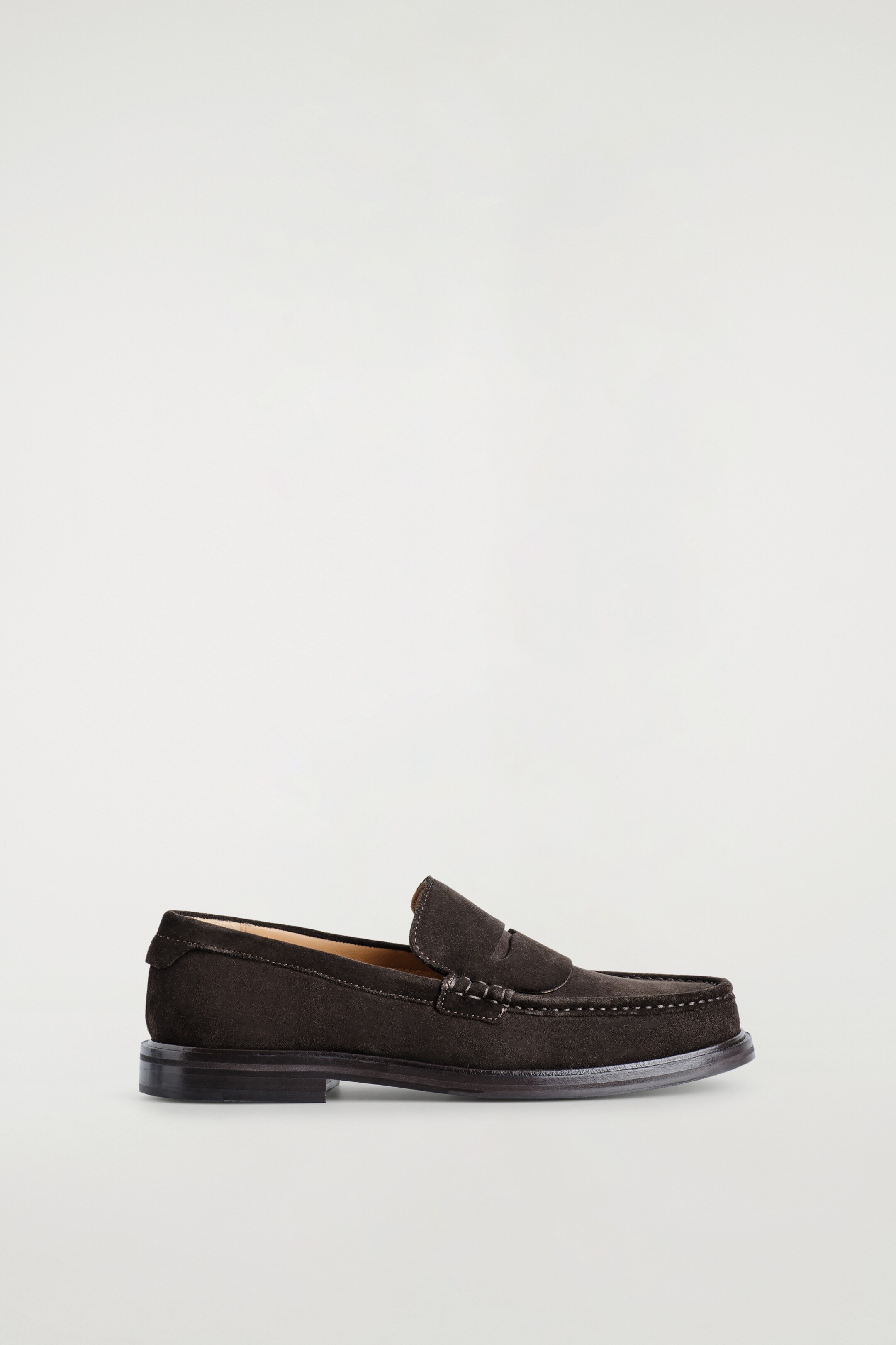 Agrandir l'image: Un mocassin en daim noir est présenté face à droite, avec une bride classique sur le cou-de-pied avec une fente. Des surpiqûres ton sur ton détaillent le bout mocassin, et la chaussure repose sur un talon bas empilé.