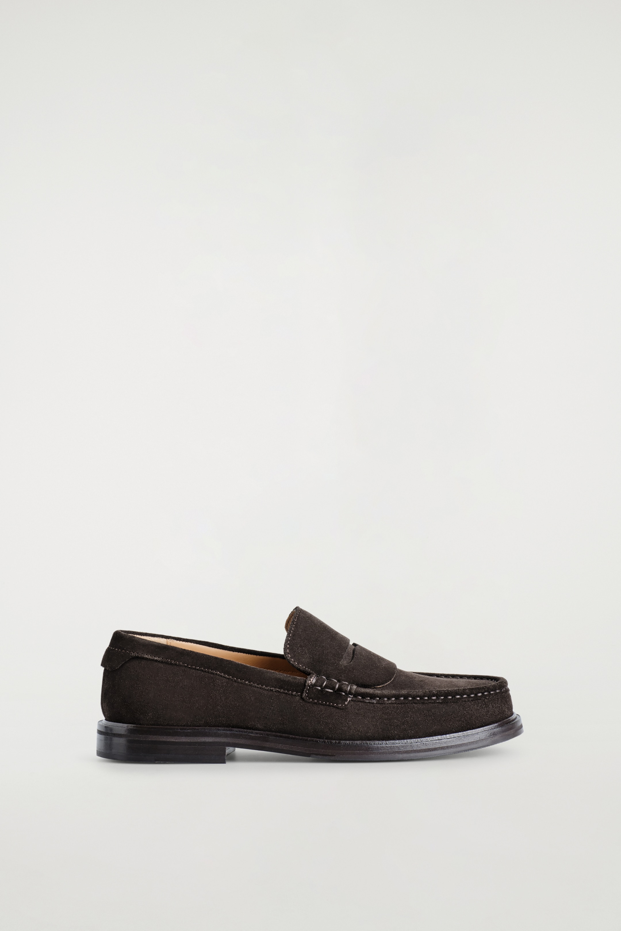 Ver imagem maior: Um mocassim de camurça preta é apresentado virado para a direita, com uma tira clássica no peito do pé com uma ranhura. A costura tonal está a detalhar a biqueira moc, e o sapato está assente num salto baixo e empilhado.