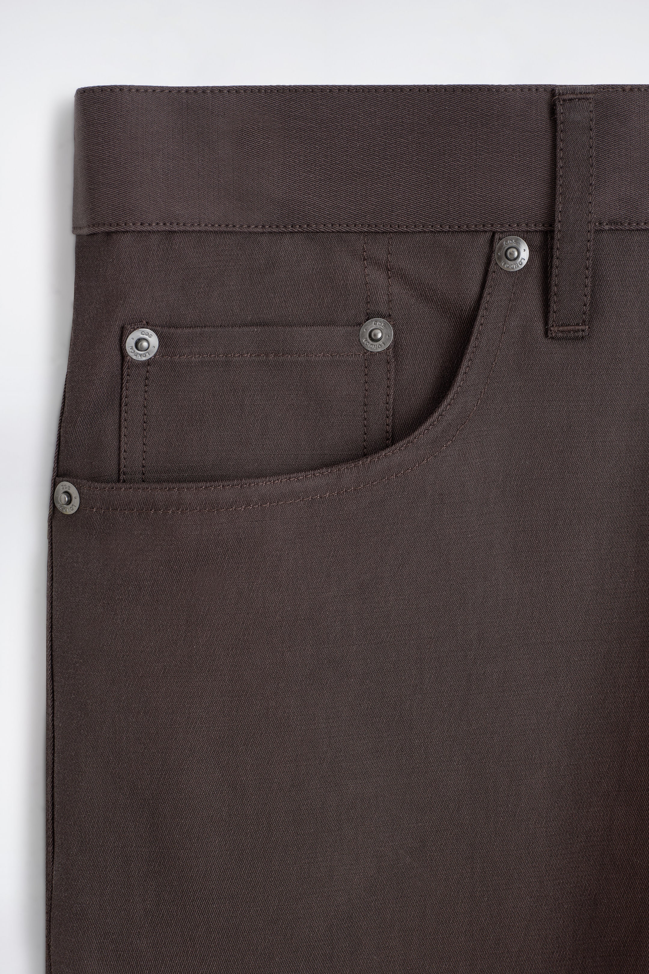 The signature regular-fit straight-leg jeans are shown in a close-up focusing on the front right pocket in a dark brown twill fabric. The design features a curved front pocket, a rectangular coin pocket with metallic rivets, and a belt loop along the waistband. The signature regular-fit straight-leg jeans are shown in a close-up focusing on the front right pocket in a dark brown twill fabric. The design features a curved front pocket, a rectangular coin pocket with metallic rivets, and a belt loop along the waistband.