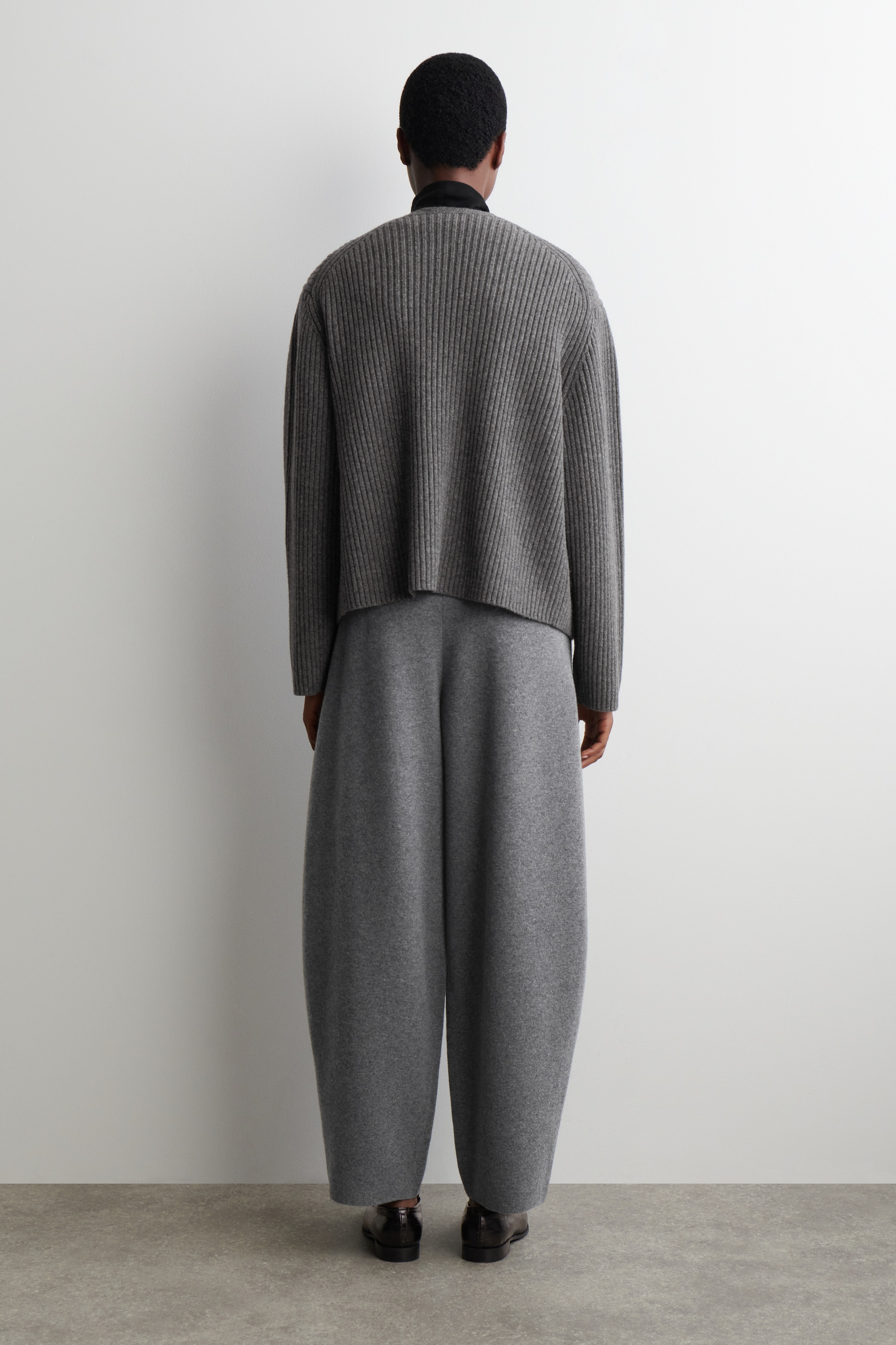 Grösseres Bild ansehen: Kohlenfarbene Hosen mit Fassbein, aus einem weichen Strickmaterial gefertigt, werden vom Model getragen. Die Hosen werden mit einem passenden grauen gerippten Pullover kombiniert, um ein abgestimmtes Set zu bilden.