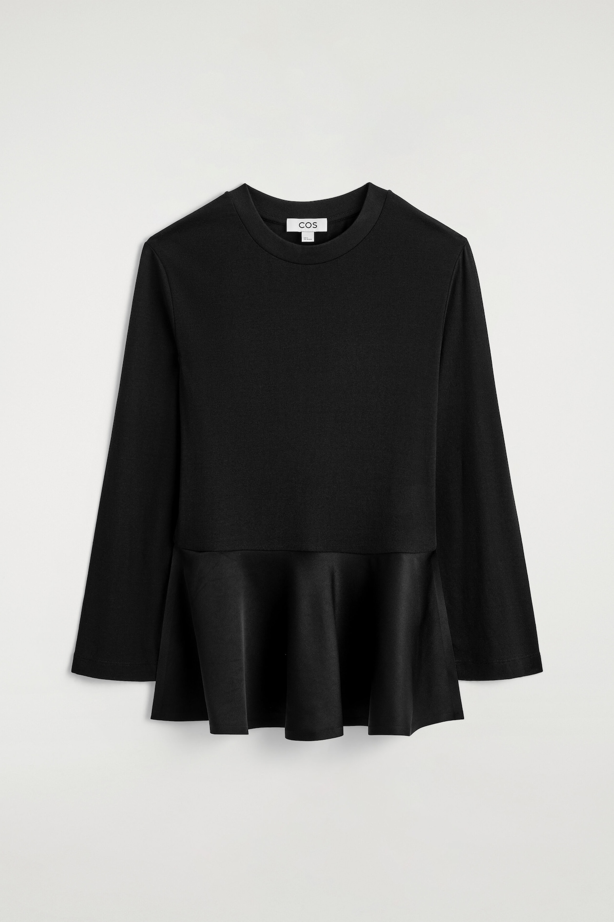 Le haut en jersey à basque en satin est présenté de face, mettant en valeur un corsage en jersey mat avec un col ras-du-cou côtelé et des manches longues. Un tissu satiné brillant contrastant forme un ourlet à basque structuré et volanté à la taille.