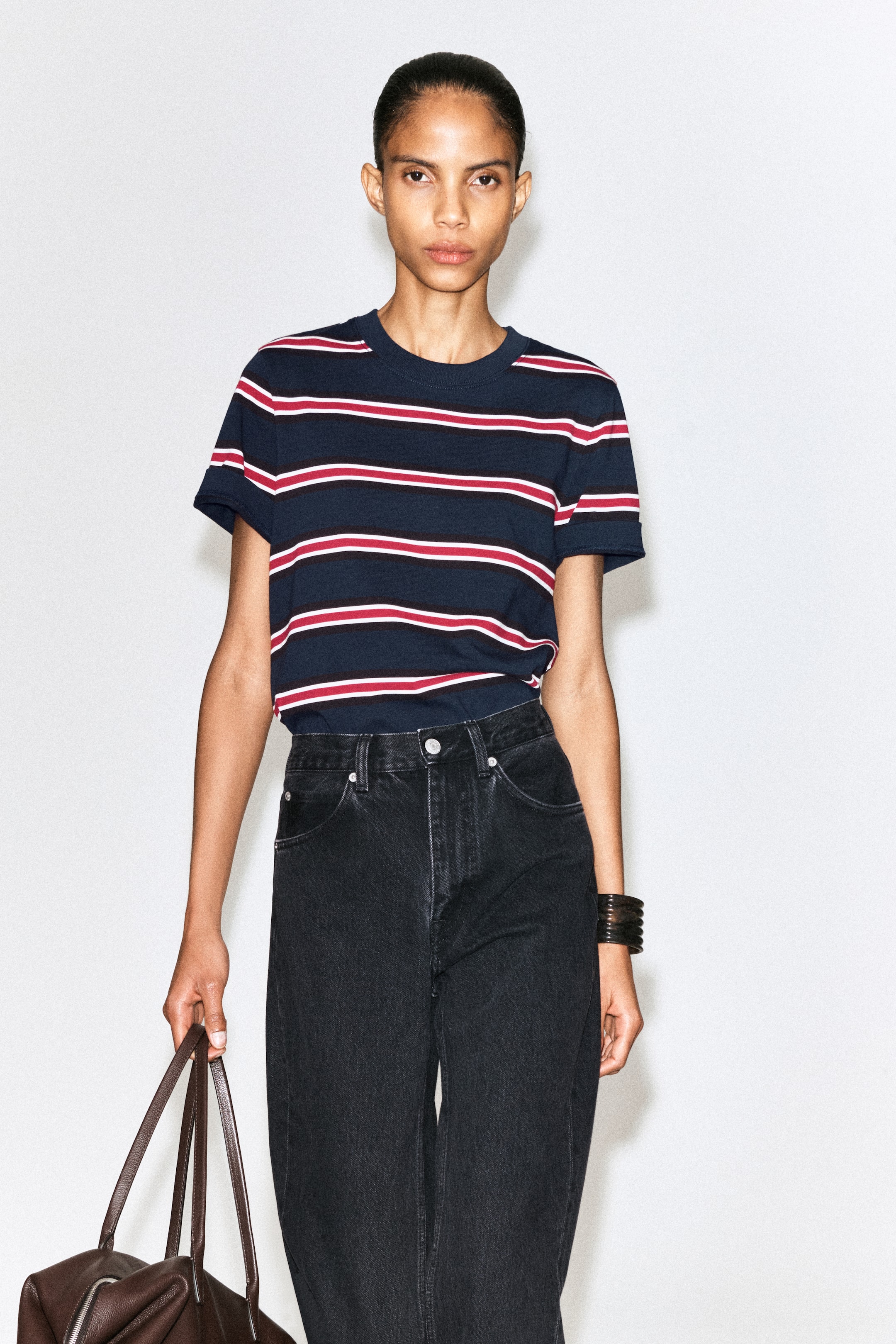 View larger image: The T-shirt features a navy blue base with horizontal red and white stripes, a crew neck, and short sleeves, and is worn tucked into dark wash jeans.