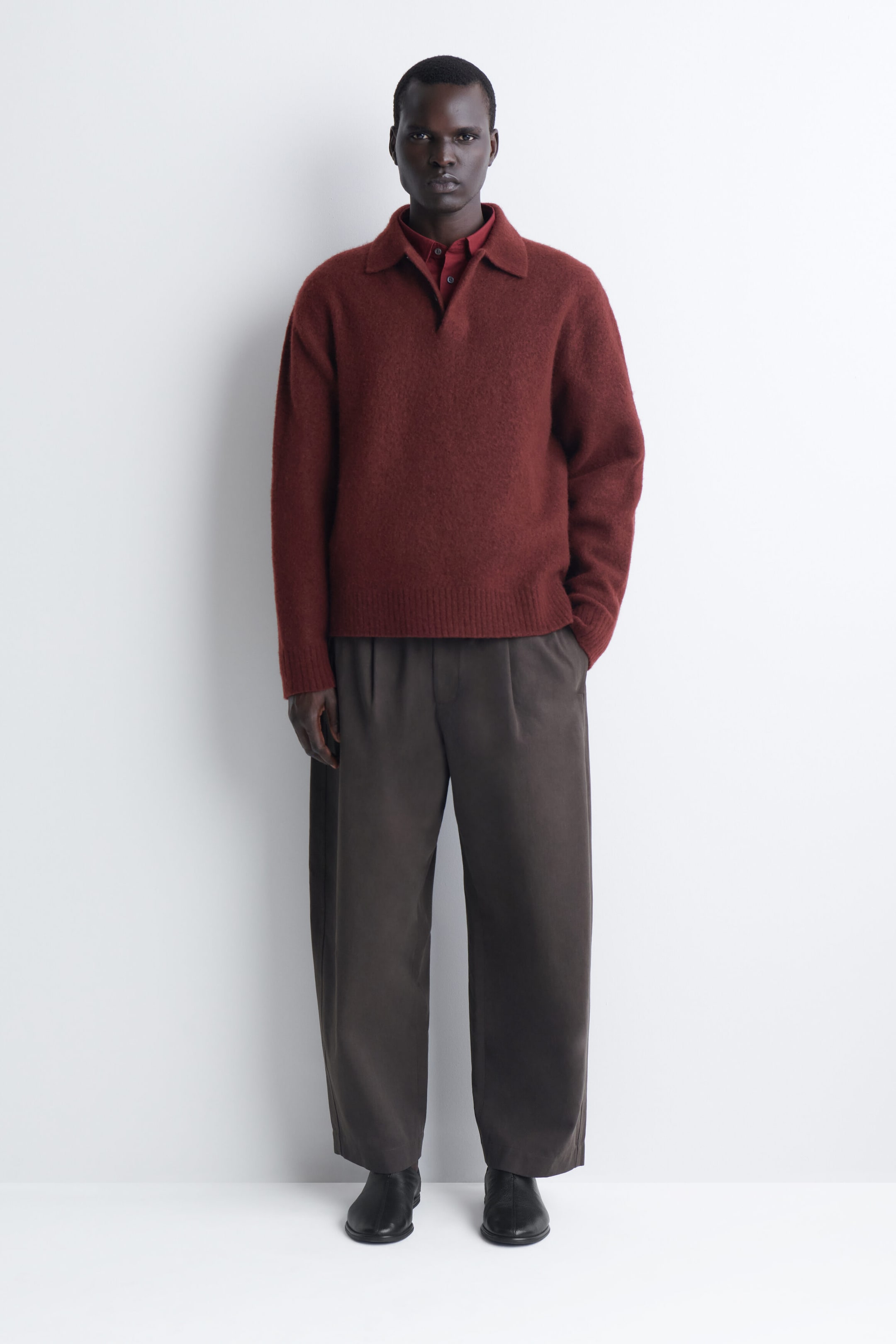 The brushed-wool polo shirt in a deep rust red is shown from the front, featuring a fuzzy, textured finish, a polo collar, and an open placket. It fits loosely, with ribbed cuffs and hem, and is layered over a matching red collared shirt. The brushed-wool polo shirt in a deep rust red is shown from the front, featuring a fuzzy, textured finish, a polo collar, and an open placket. It fits loosely, with ribbed cuffs and hem, and is layered over a matching red collared shirt.