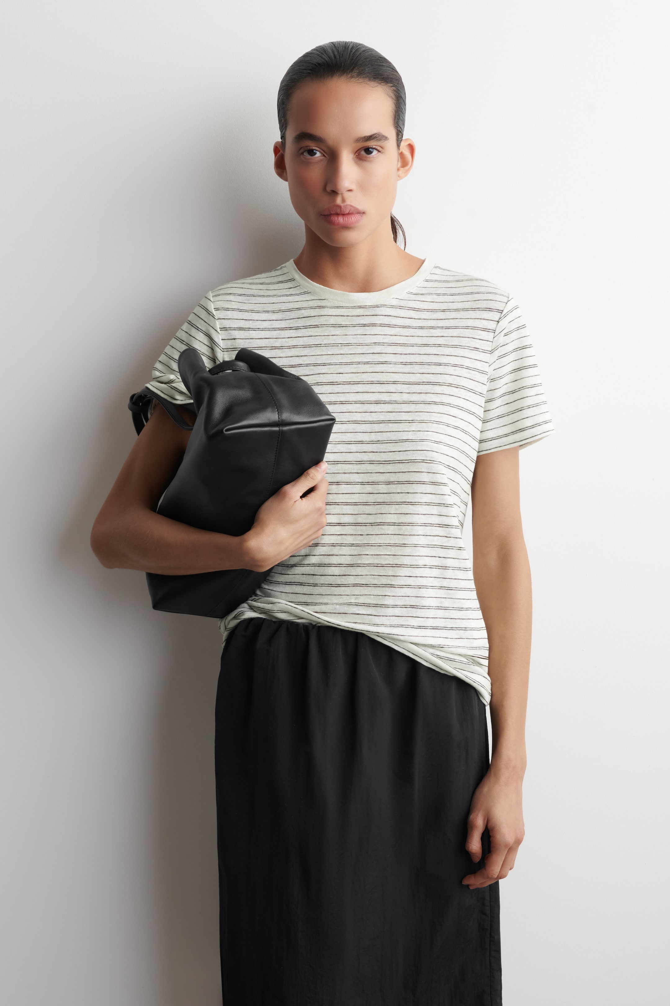 הצגת תמונה גדולה יותר: "תיק עור שחור מוחזק ביד, מציג את צורתו הרכה והמלבנית עם תחתית שטוחה, חלק עליון מכווץ וידית אחת מעוגלת."