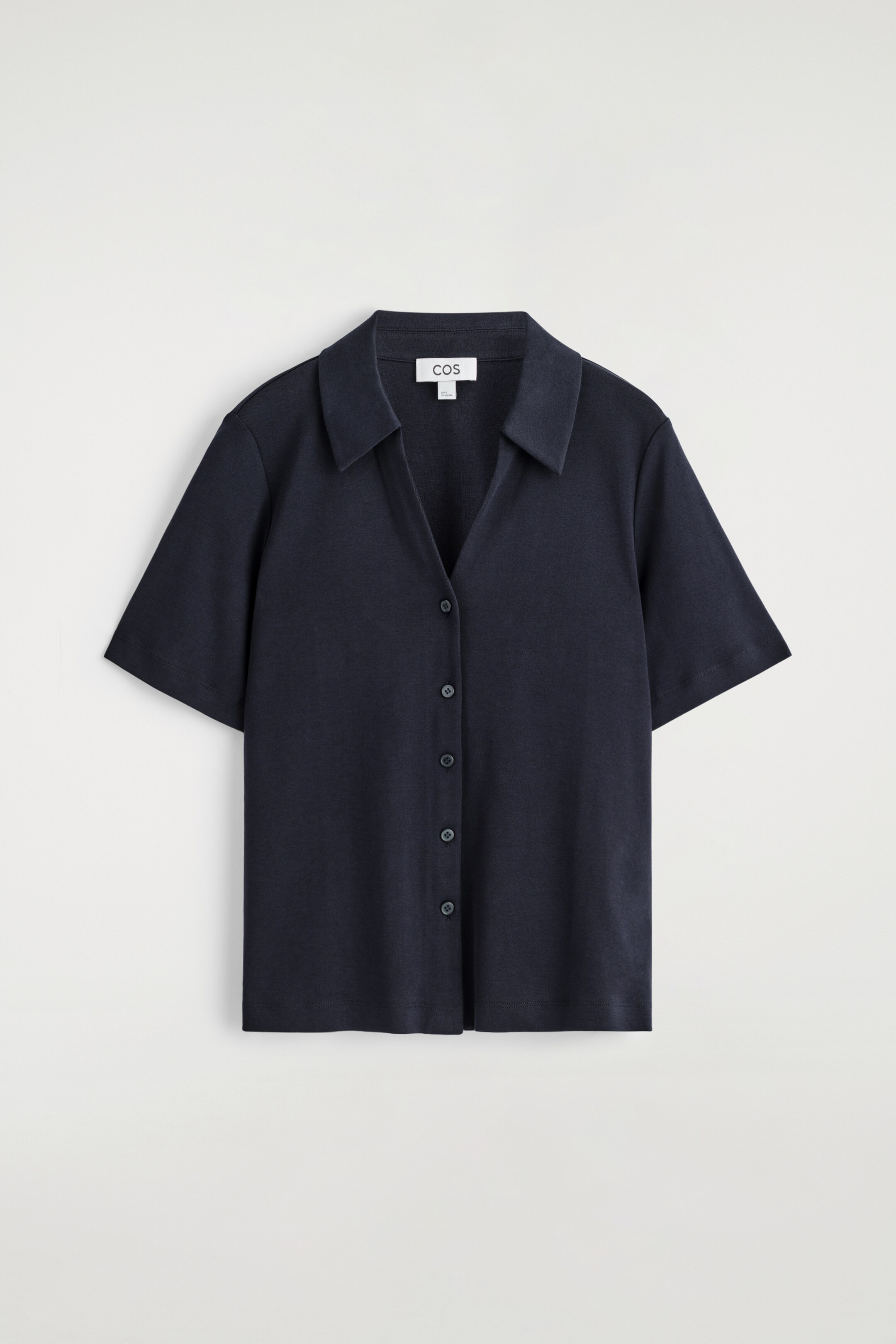 Agrandir l'image: Une chemise de villégiature en tricot bleu foncé présente son devant, avec un col ouvert, des manches courtes et une fermeture complète avec des boutons ton sur ton. Une petite étiquette de marque blanche est visible à l'arrière du cou.