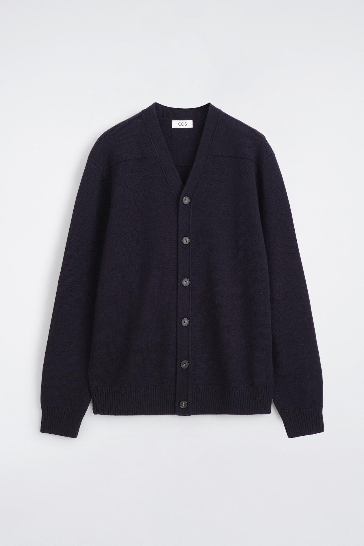 A dark blue cardigan is shown from the front, featuring a V-neckline and a six-button front fastening with dark circular buttons. It has long sleeves with ribbed cuffs, a ribbed hem, and knitted shoulder panels.