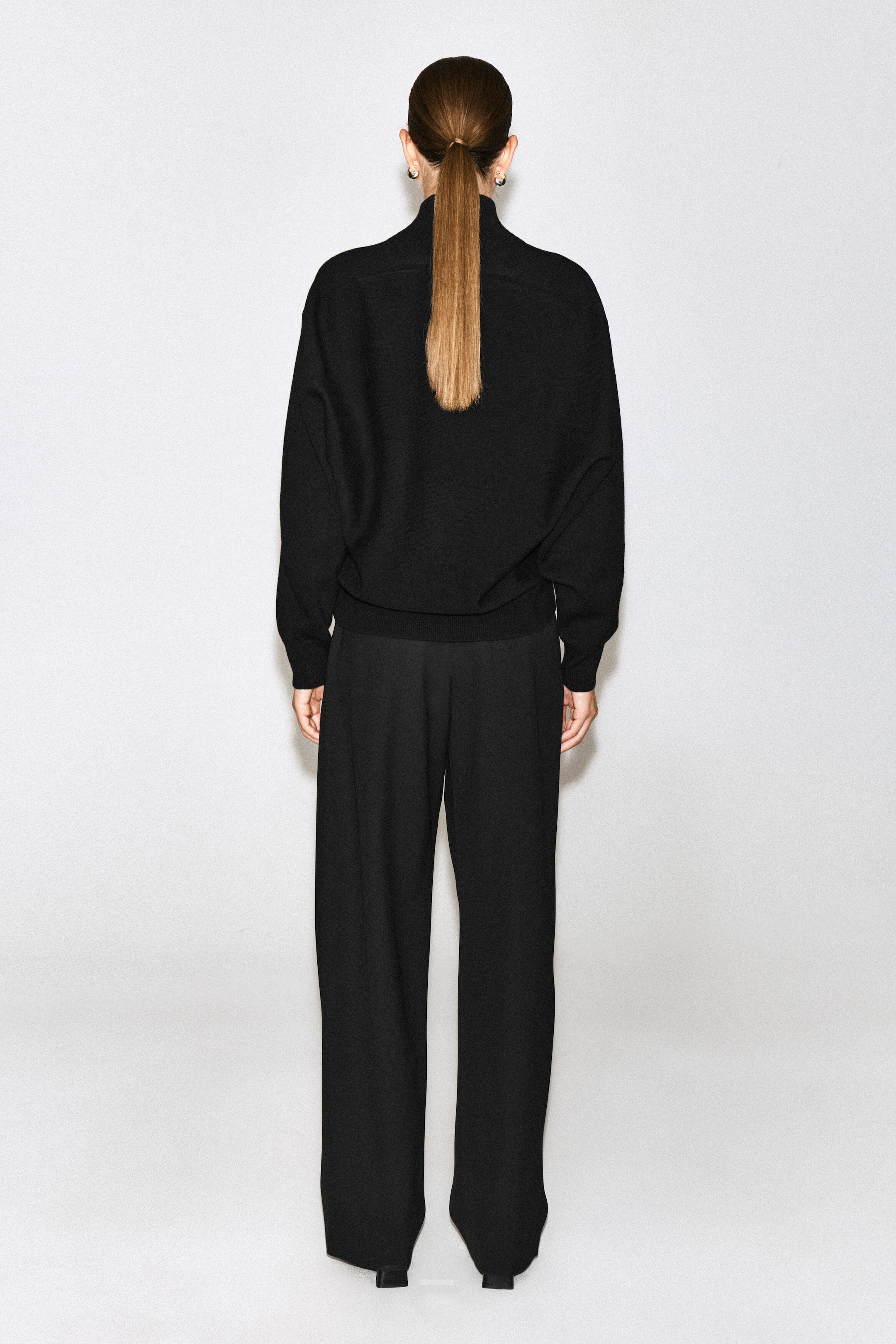 Un chandail noir en laine bouillie à col cheminée est porté par le mannequin, vu de dos. Le vêtement à manches longues présente un col montant ainsi que des poignets et un ourlet côtelés, et il est assorti à un pantalon noir ample à jambes larges. Un chandail noir en laine bouillie à col cheminée est porté par le mannequin, vu de dos. Le vêtement à manches longues présente un col montant ainsi que des poignets et un ourlet côtelés, et il est assorti à un pantalon noir ample à jambes larges.