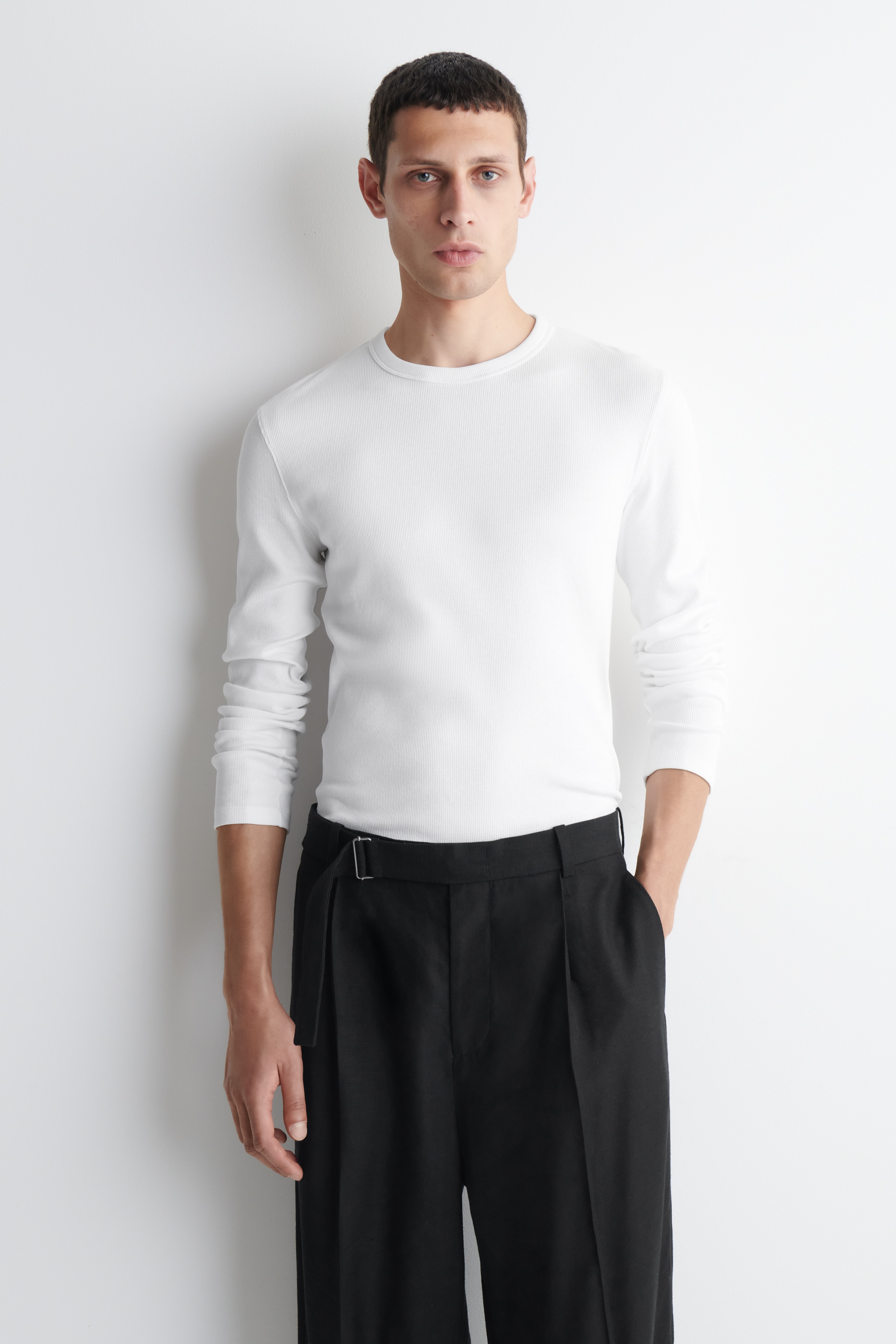 Un t-shirt blanc à manches longues est présenté de face, avec une texture finement côtelée, un col rond et une coupe ajustée et près du corps.