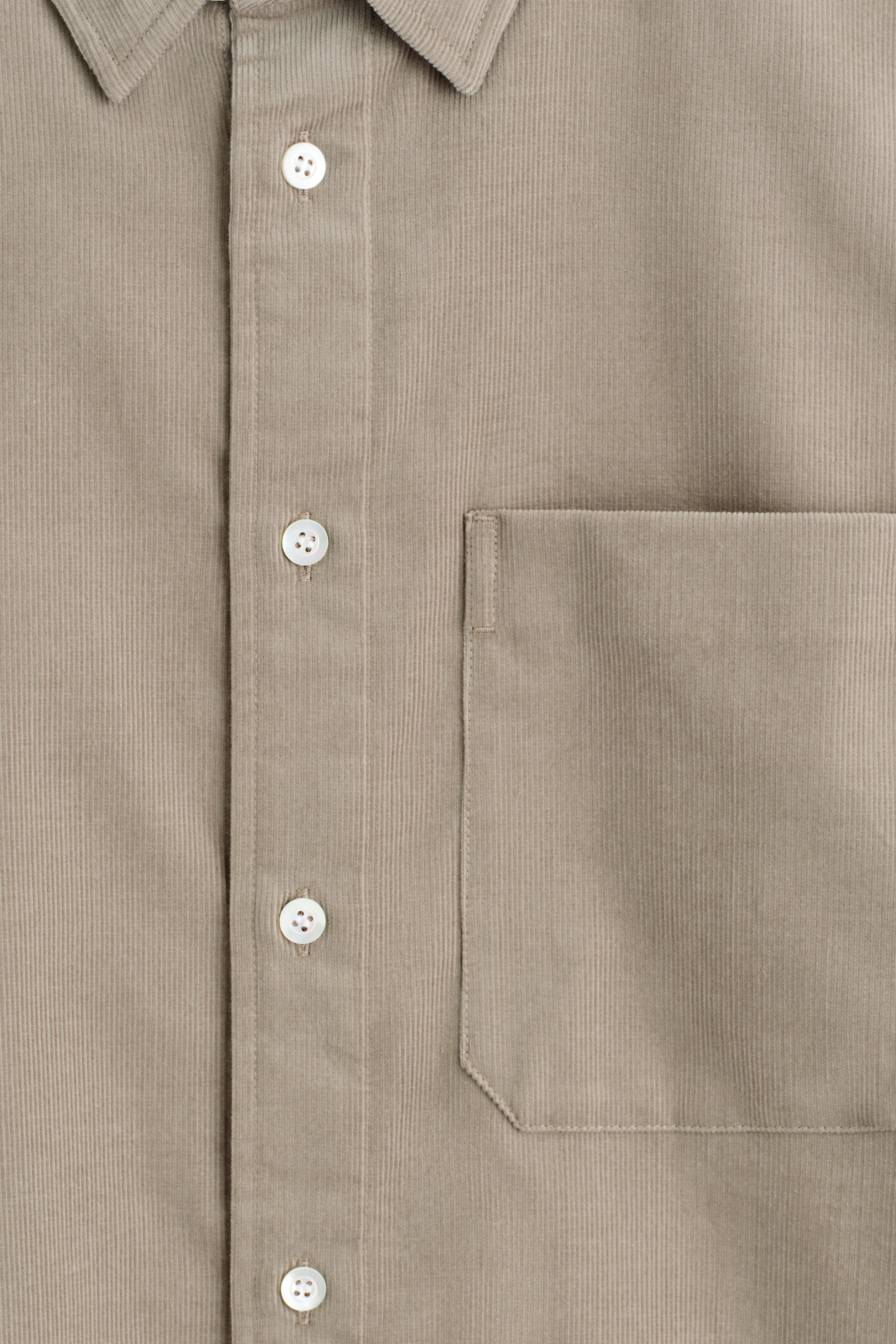 Agrandir l'image: Le DEVANT d'une chemise en velours côtelé brun clair affiche sa texture côtelée verticale distincte. Elle présente une patte de boutonnage centrale avec des boutons en nacre blanche et une seule poche poitrine plaquée sur le côté gauche.