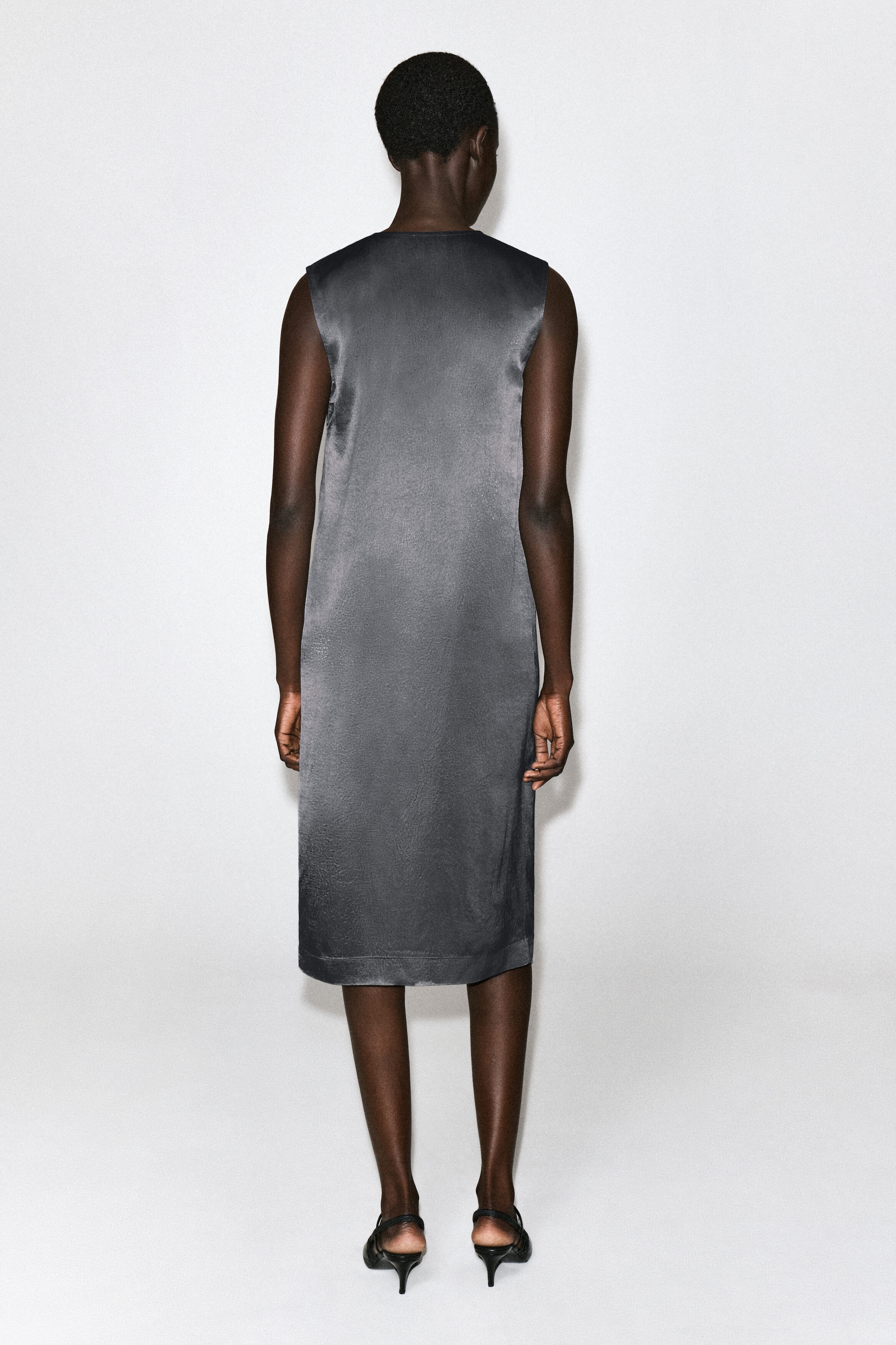 The grey Beaded Satin V-Neck Midi Dress is shown from the back in a straight-cut, sleeveless silhouette. The lustrous satin fabric falls to midi length, creating a clean, minimalist drape. The grey Beaded Satin V-Neck Midi Dress is shown from the back in a straight-cut, sleeveless silhouette. The lustrous satin fabric falls to midi length, creating a clean, minimalist drape.