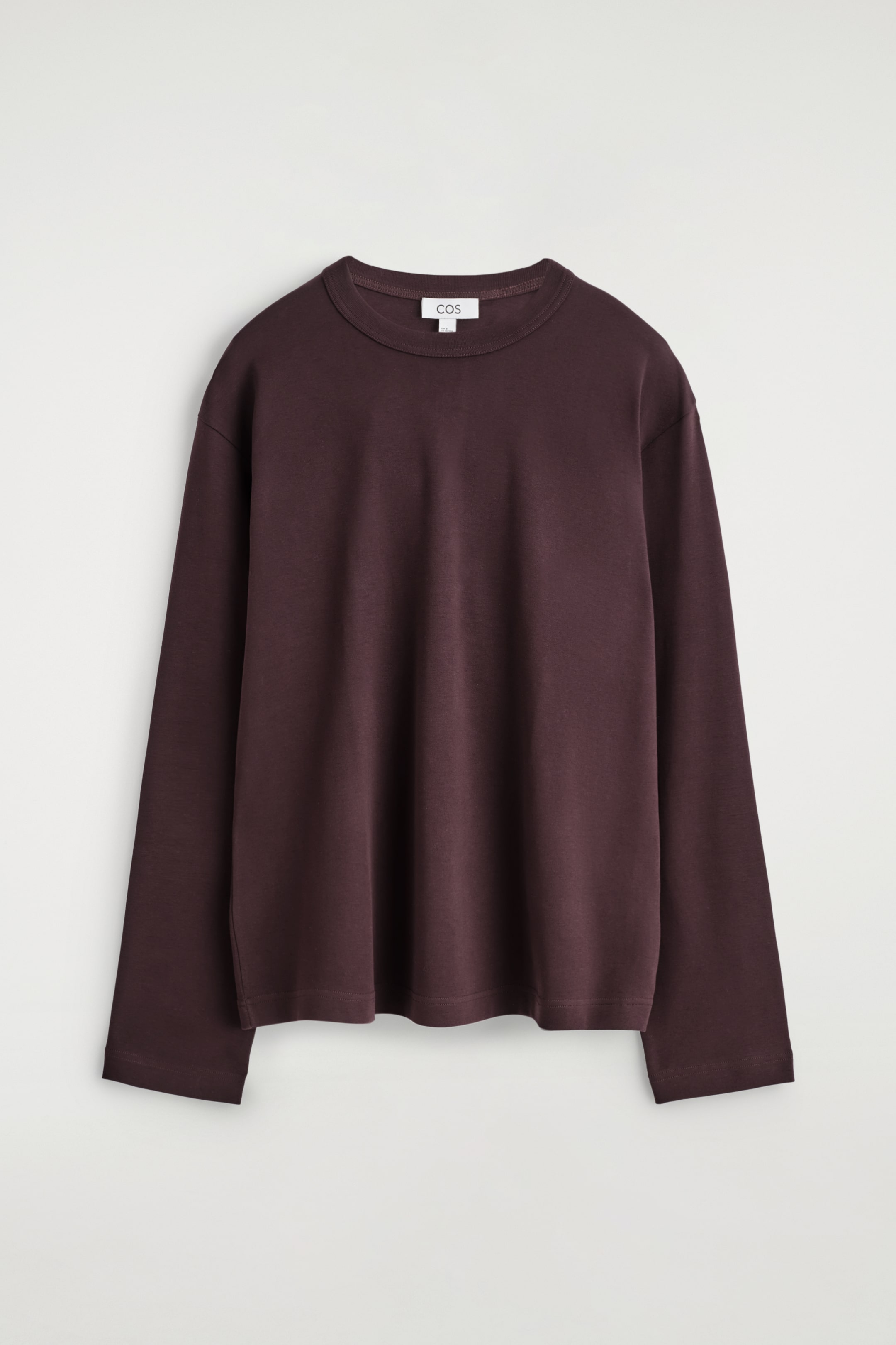 Ver imagen más grande: Una camiseta de manga larga de color marrón oscuro se muestra desde el frente, con un ajuste relajado, un cuello redondo clásico y un dobladillo recto. Una pequeña etiqueta blanca con la inscripción 'COS' es visible en la parte trasera del cuello.