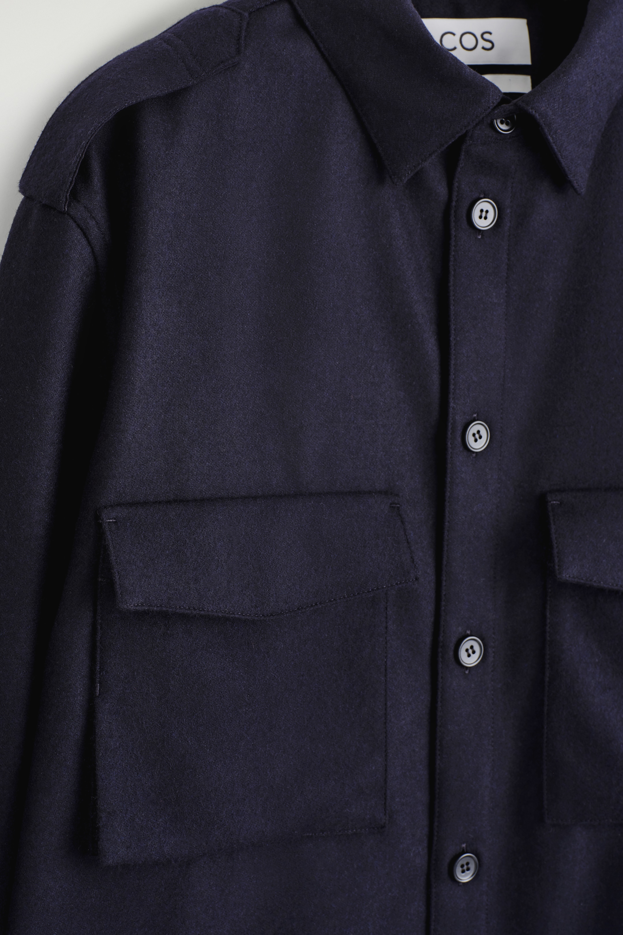 Ingrandisci l'immagine: Una camicia utility blu navy viene presentata dal davanti, caratterizzata da un colletto classico, un'abbottonatura con bottoni di colore chiaro, due grandi tasche applicate sul petto con patte e spalline sulle spalle. Il tessuto ha una texture morbida e opaca.