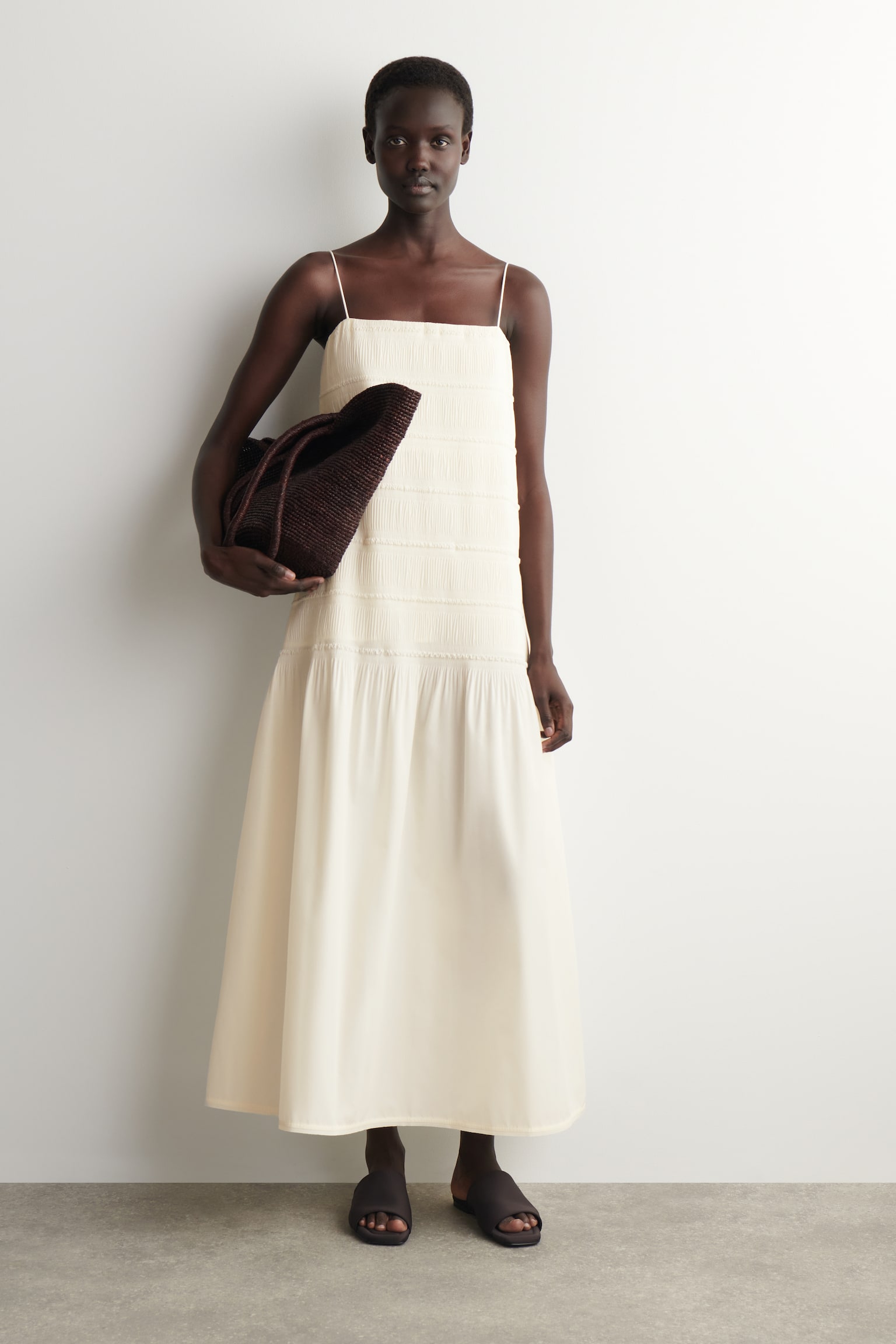 A cream maxi dress featuring thin spaghetti straps and a textured, shirred bodice extending to the waist. The skirt flows smoothly from the waist to ankle length. - 1