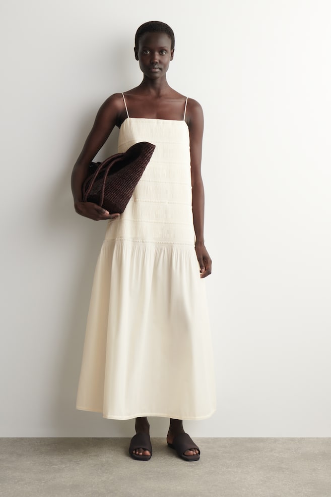 Un vestido maxi color crema con finos tirantes de espagueti y un corpiño texturizado y fruncido que se extiende hasta la cintura. La falda cae suavemente desde la cintura hasta el largo del tobillo. - 1