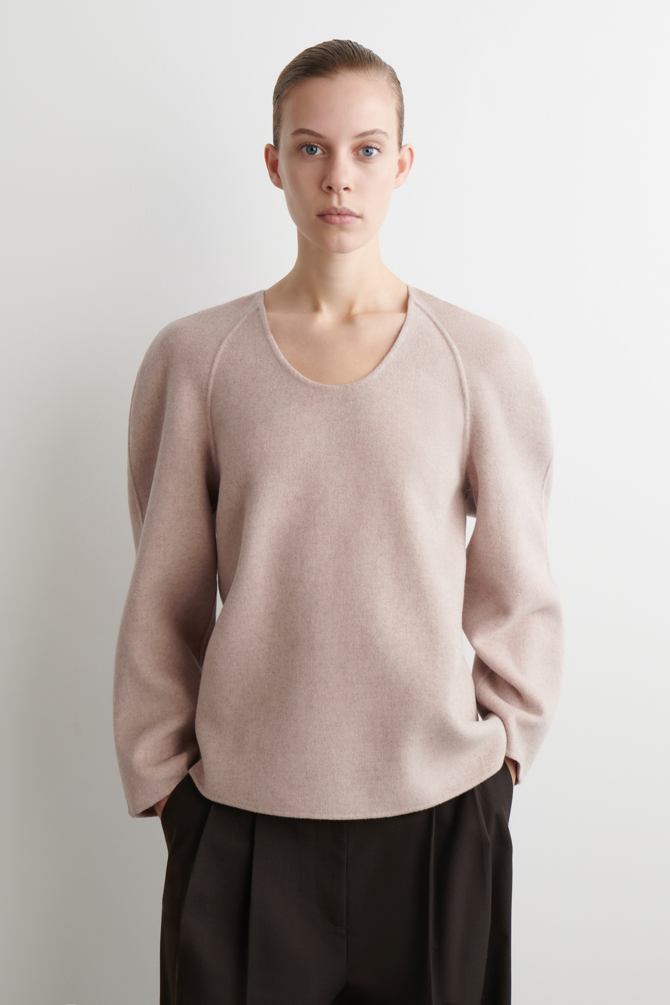 View larger image: A light pink top is being presented, facing forward, featuring a wide scoop neckline, raglan sleeves, and a relaxed, boxy fit. It is displaying a smooth fabric and a straight hemline that is falling loosely over the hips.