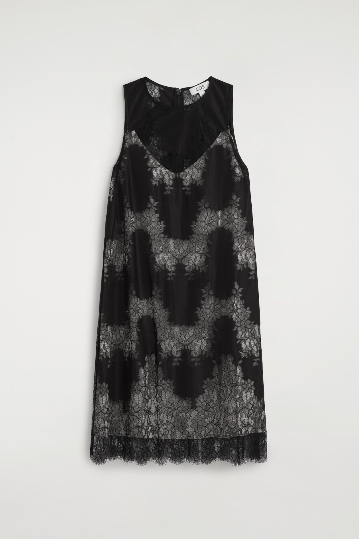 A sleeveless lace midi dress is shown from the front, featuring a black floral lace overlay with a contrasting light-grey patterned underlayer. The dress features a high round neckline with a sheer lace yoke and a relaxed silhouette, finishing with a scalloped eyelash lace hem.