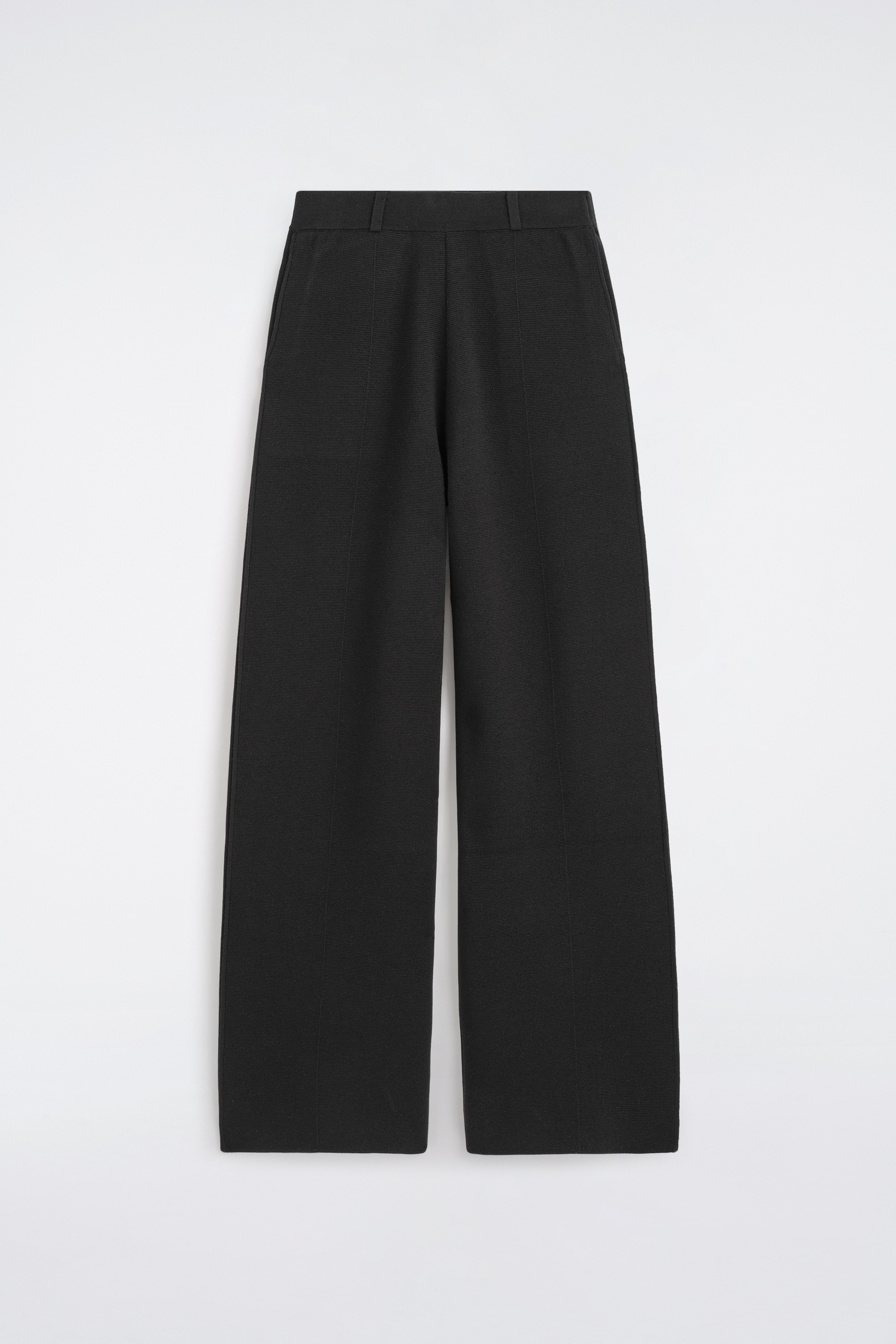 I pantaloni dritti in misto lana merino sono mostrati frontalmente, con una silhouette rilassata a taglio dritto in nero. I pantaloni arrivano a tutta lunghezza sopra scarpe nere e sono abbinati a un cardigan con bottoni coordinato, sovrapposto alla cintura.