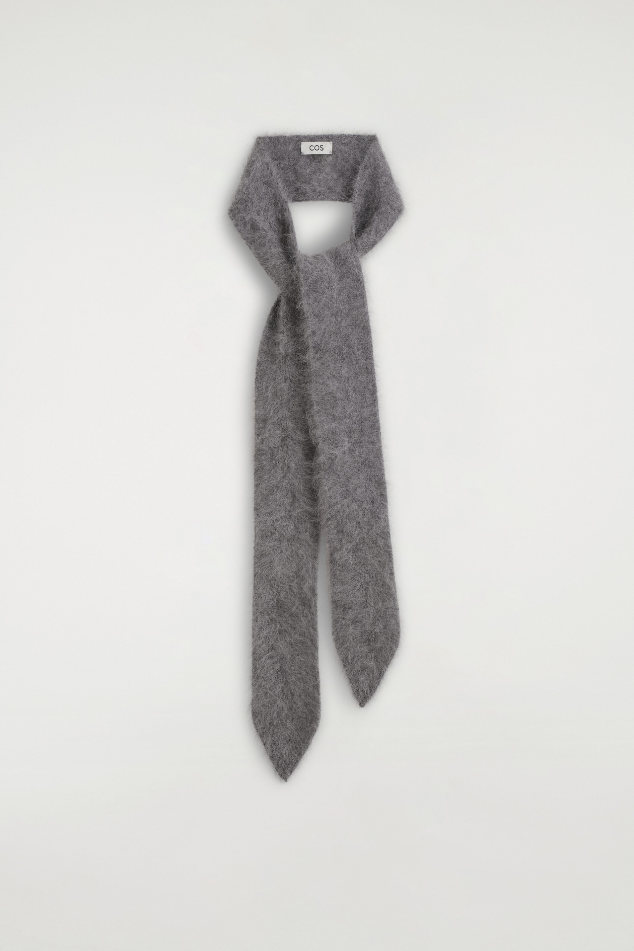 A gray brushed wool knit scarf is shown from the front, styled in a loop that mimics the shape of a classic necktie. The fuzzy, textured scarf hangs straight down with its ends crossed over and finishing in pointed tips.