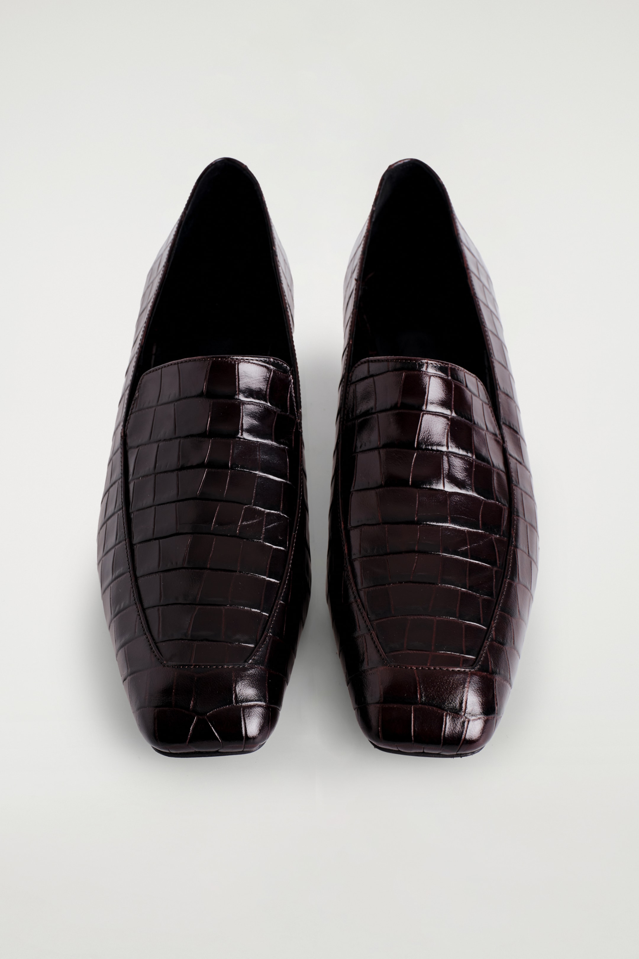 Agrandir l'image: Une paire de mocassins marron foncé avec une texture effet crocodile embossée est présentée vue de dessus, mettant en valeur leur bout subtilement carré.