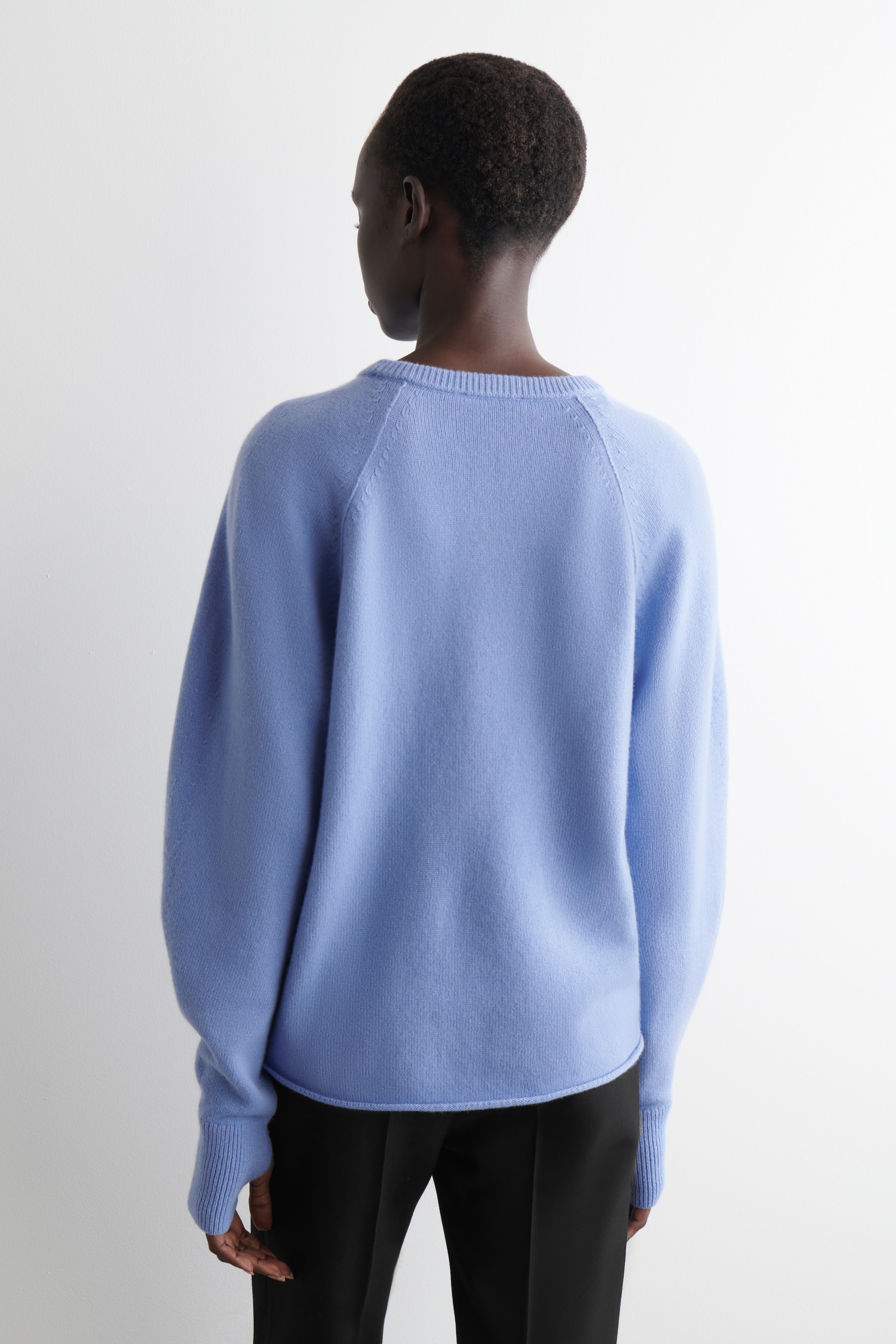 Visualizza immagine più grande: Un maglione azzurro chiaro in maglia fine viene visto da dietro, mostrando la sua vestibilità regolare, il girocollo a coste, le maniche raglan, i polsini a coste con fori per i pollici e l'orlo arrotolato.