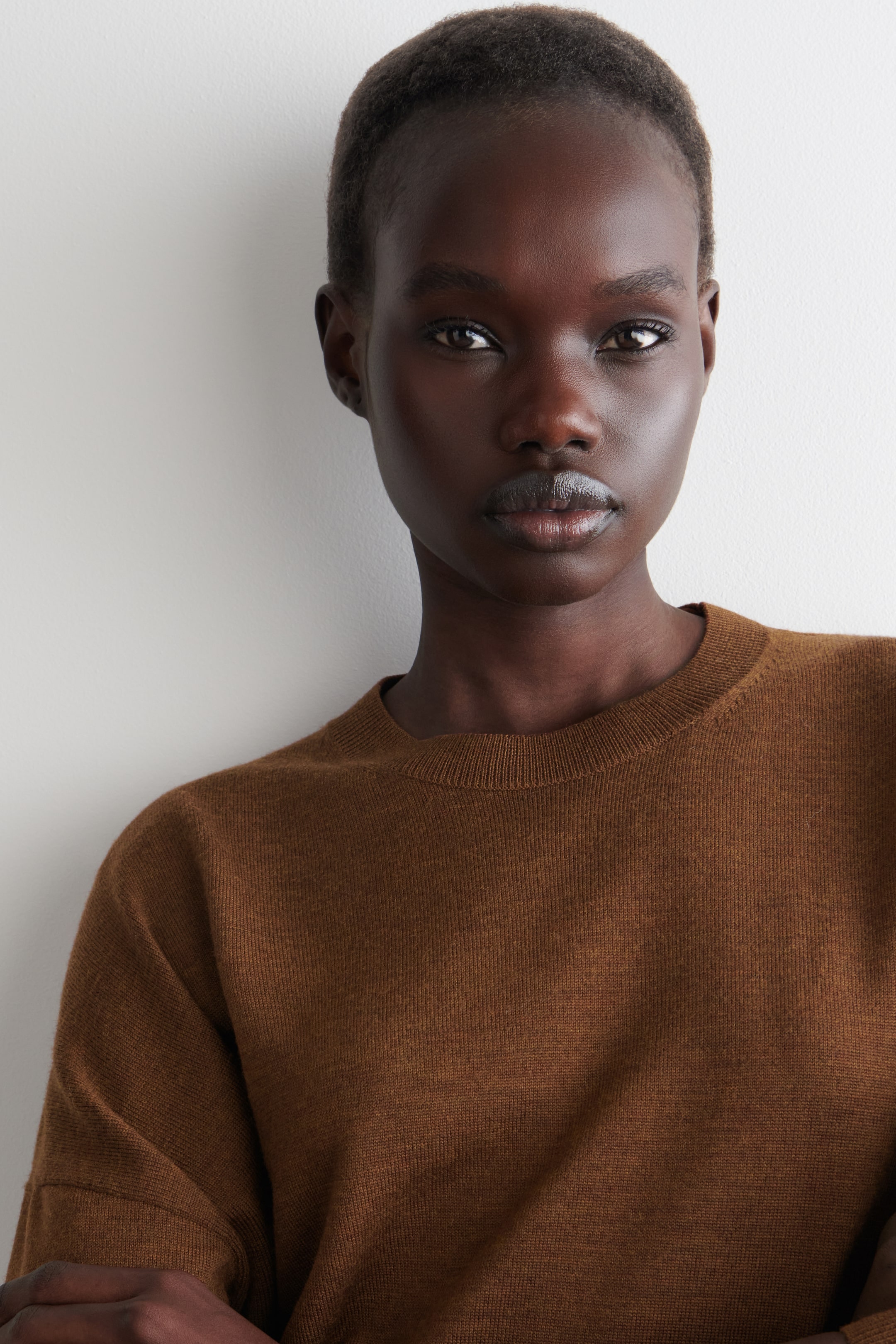 Agrandir l'image: Un haut en tricot marron à manches longues est porté, vu de face et légèrement incliné vers la droite, mettant en valeur sa coupe décontractée sur les épaules. Il présente un col rond avec une finition côtelée subtile et une texture en tricot fin et lisse.