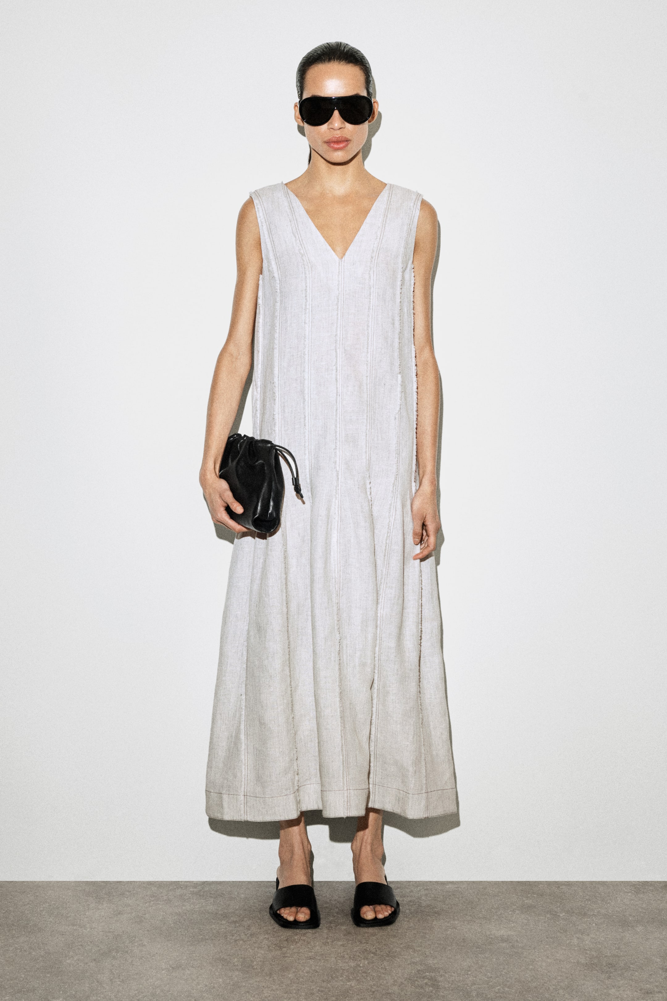 Agrandir l'image: La robe est présentée de face, arborant un design gris clair, sans manches, de longueur midi avec un décolleté en V, un panneau vertical avec des détails à bords bruts, et un ourlet évasé.