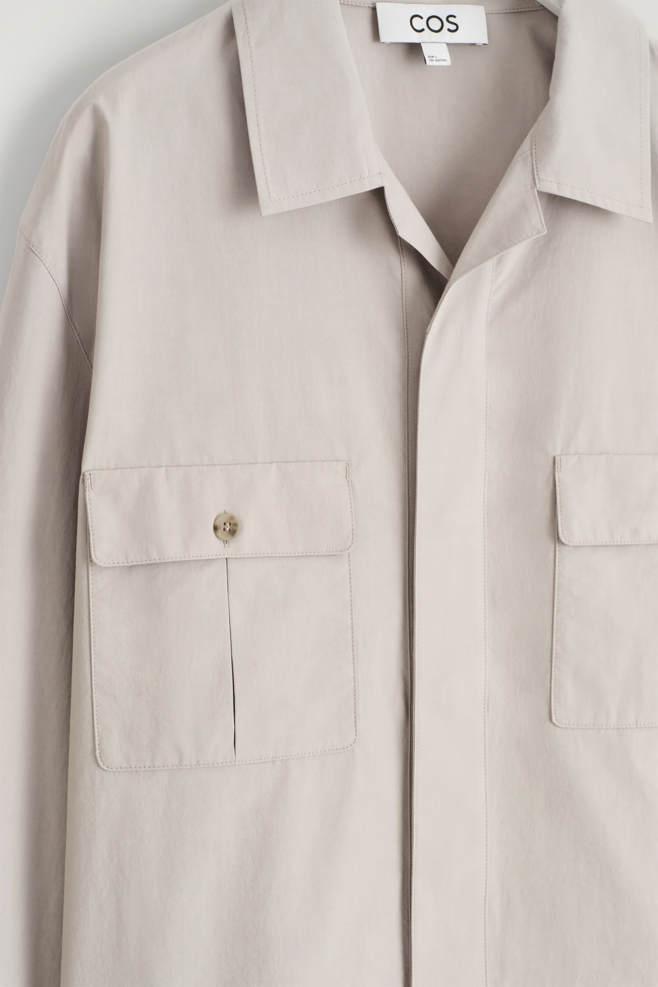 Größeres Bild anzeigen: Eine hellbeige Overshirt wird von vorne präsentiert, mit einem Kentkragen, einer verdeckten Knopfleiste und zwei großen Brusttaschen mit Patte, von denen eine einen hellen Knopf zeigt.