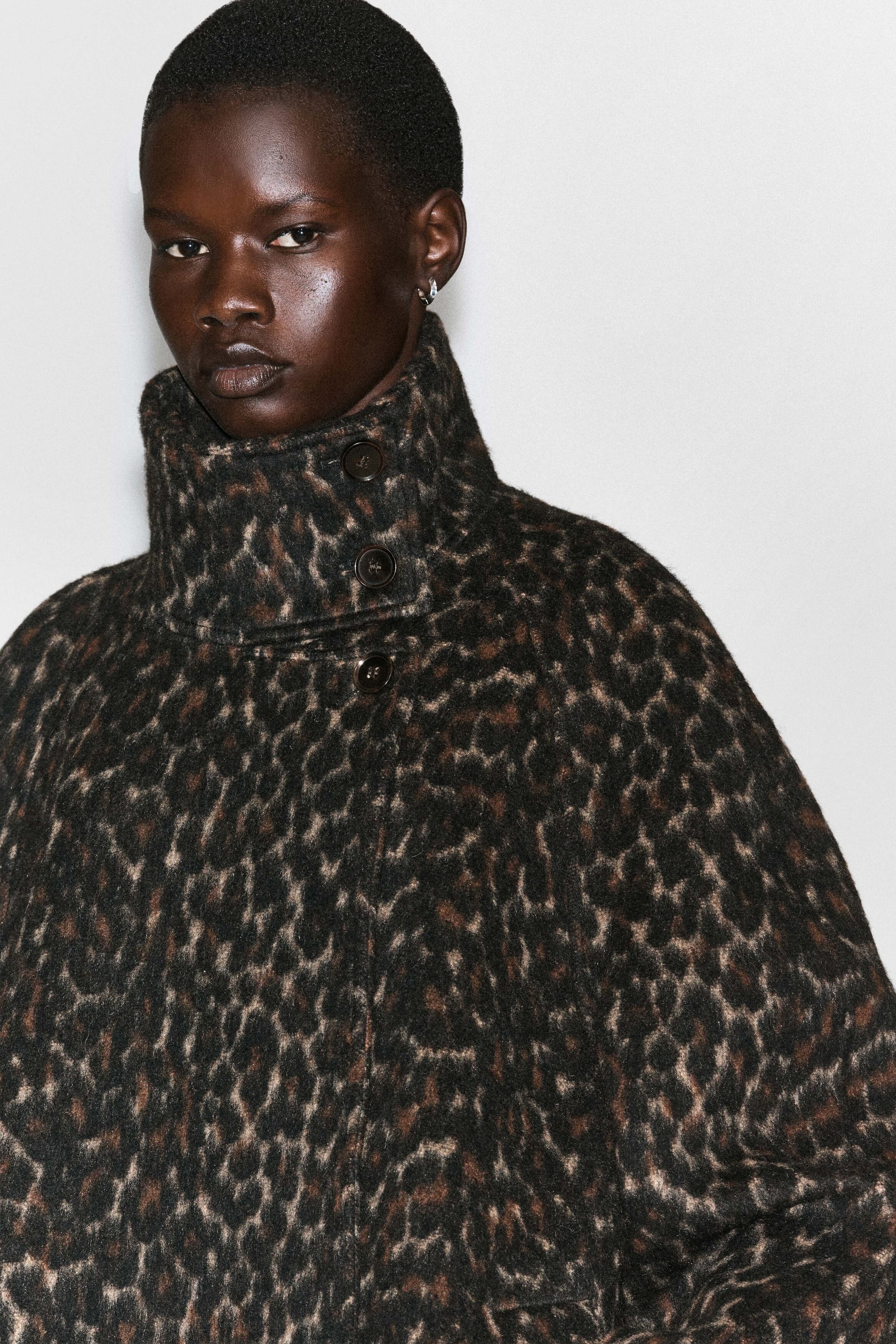 Ein Mantel aus Wollmischung mit Leopardenmuster und hohem, geknöpftem Stehkragen wird vom Model getragen. Der Mantel ist bis zum Kinn zugeknöpft dargestellt und hebt so sein strukturiertes Gewebe und das dunkle Animal-Print-Muster hervor. Ein Mantel aus Wollmischung mit Leopardenmuster und hohem, geknöpftem Stehkragen wird vom Model getragen. Der Mantel ist bis zum Kinn zugeknöpft dargestellt und hebt so sein strukturiertes Gewebe und das dunkle Animal-Print-Muster hervor.