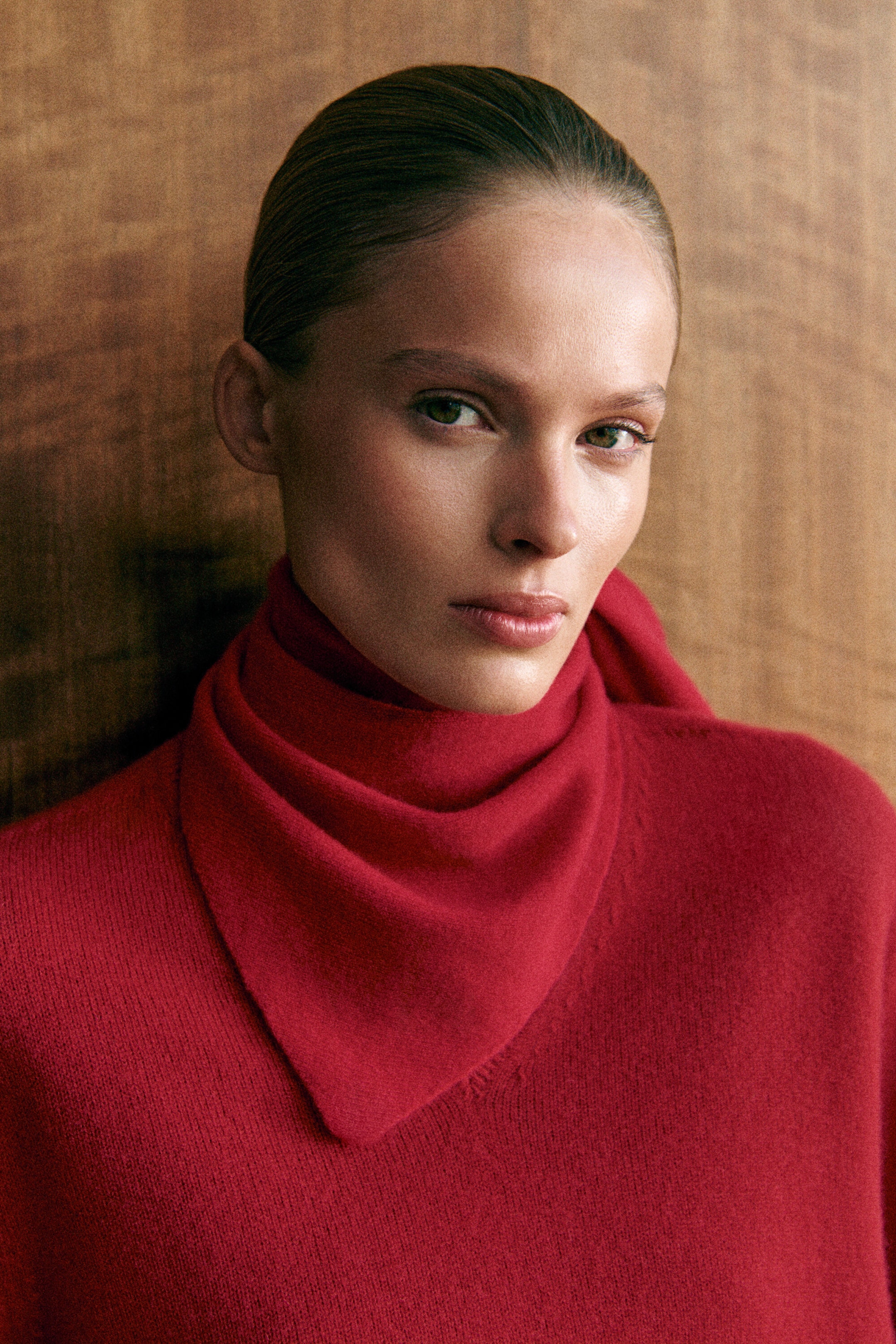 The red cashmere triangle scarf is wrapped around the neck, with its pointed corner draped forward, layered over a matching red sculpted cashmere V-neck sweater shown from the front. The red cashmere triangle scarf is wrapped around the neck, with its pointed corner draped forward, layered over a matching red sculpted cashmere V-neck sweater shown from the front.