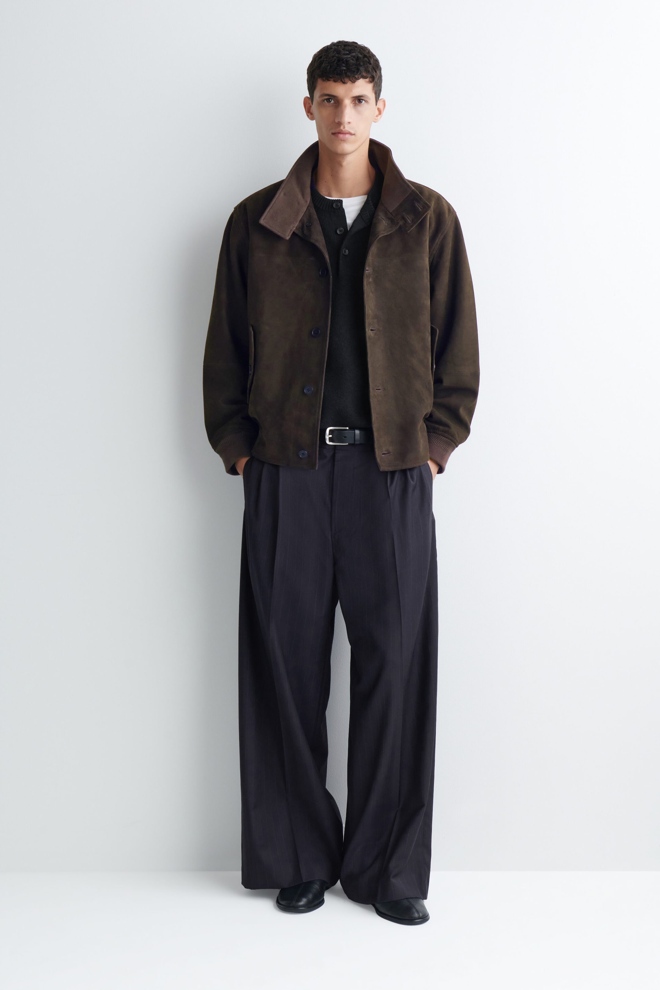 Pantalon plissé à jambe large et coupe décontractée, en gris foncé, porté par le mannequin, avec une ceinture en cuir noire à la taille. Le pantalon présente de profondes pinces à l’avant et une silhouette fluide et ample qui tombe légèrement sur des chaussures en cuir noir. Pantalon plissé à jambe large et coupe décontractée, en gris foncé, porté par le mannequin, avec une ceinture en cuir noire à la taille. Le pantalon présente de profondes pinces à l’avant et une silhouette fluide et ample qui tombe légèrement sur des chaussures en cuir noir.