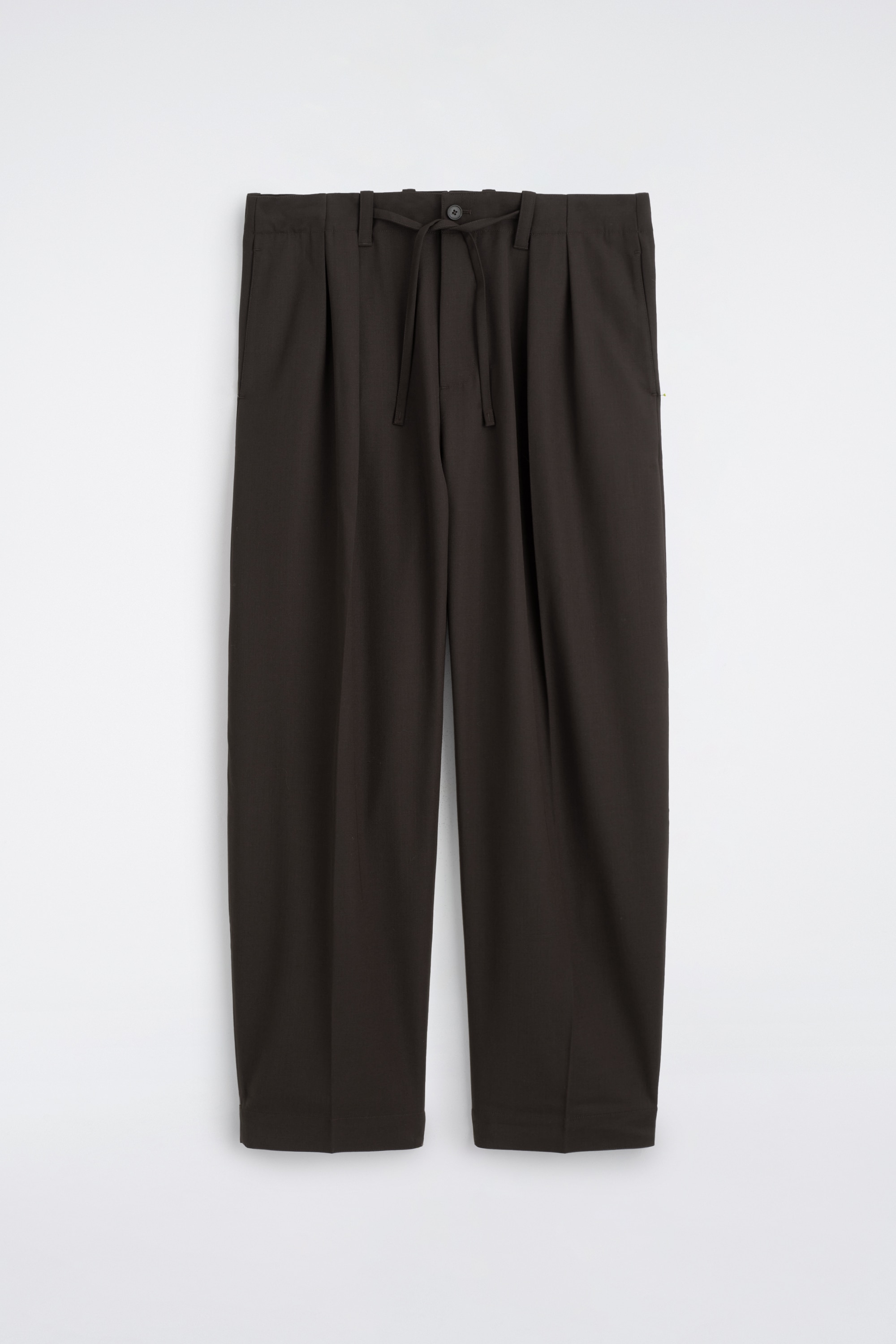 Un modÃ¨le se tient de face, portant une veste en cuir marron foncÃ© dotÃ©e dâun col Ã  revers, de fermetures boutonnÃ©es et dâune taille Ã©lastiquÃ©e. La veste est portÃ©e sur une chemise boutonnÃ©e gris charbon et associÃ©e Ã  un pantalon marron foncÃ© ample Ã  jambes larges.