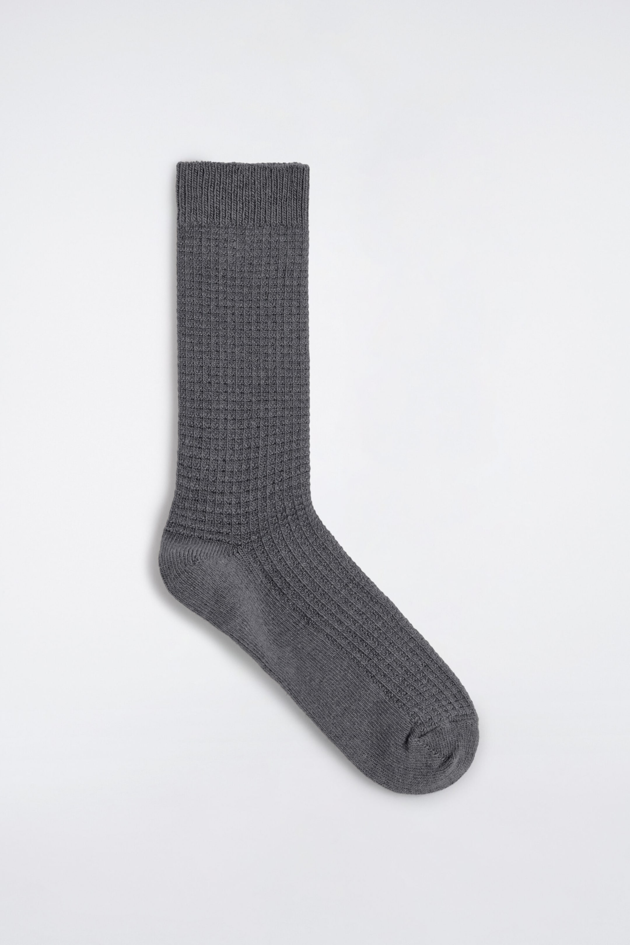 Eine graue Socke liegt flach in seitlicher Profilansicht und zeigt ihre strukturierte Waffelstrick-Optik. Das Design umfasst einen gerippten Bund am oberen Rand, einen Waffelmuster-Schaft und Spann sowie eine glatt gestrickte Ferse und Spitze. Eine graue Socke liegt flach in seitlicher Profilansicht und zeigt ihre strukturierte Waffelstrick-Optik. Das Design umfasst einen gerippten Bund am oberen Rand, einen Waffelmuster-Schaft und Spann sowie eine glatt gestrickte Ferse und Spitze.