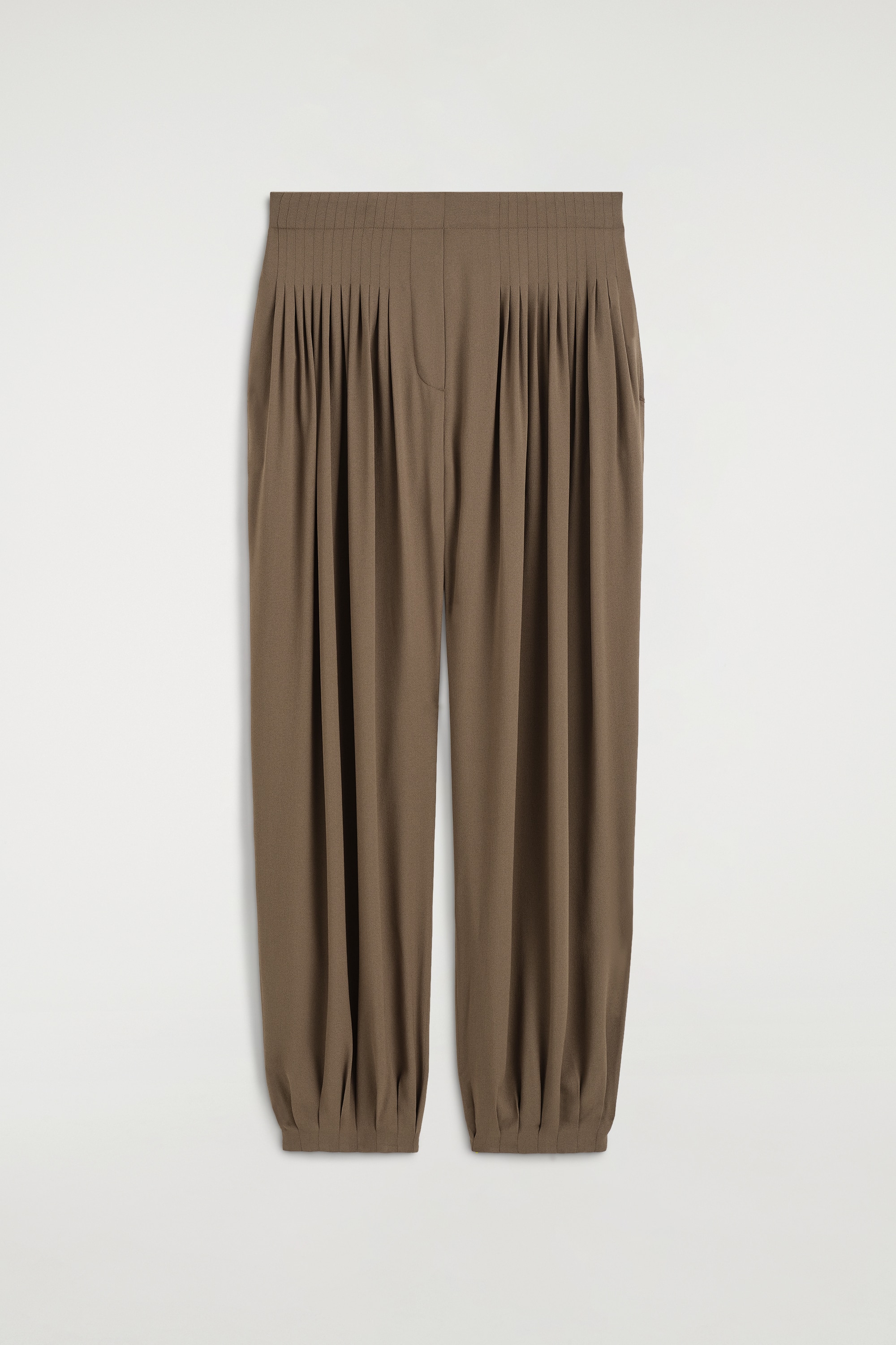 Le mannequin porte un pantalon ballon plissÃ© en crÃªpe marron, Ã  la silhouette dÃ©contractÃ©e avec des plis Ã  la taille et des chevilles froncÃ©es. Le pantalon est associÃ© Ã  une veste noire croisÃ©e et Ã  des sandales noires ouvertes Ã  lâavant type mules.